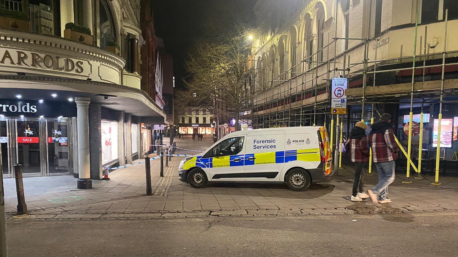 Police forensic van outside a taped off area of a street which is in front of a department store. 