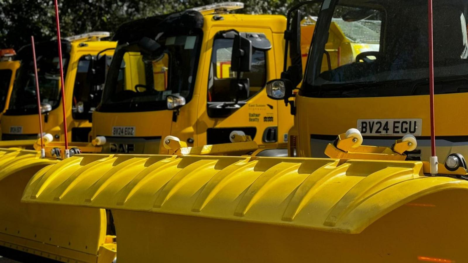 Three bright yellow gritter vehicles are parked in a row. 