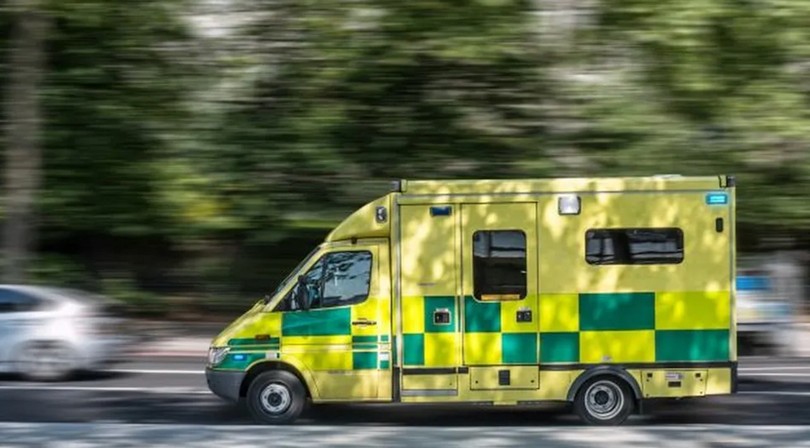 A Northern Ireland Ambulance driving on a road with the trees in the background blurred to give an element of motion