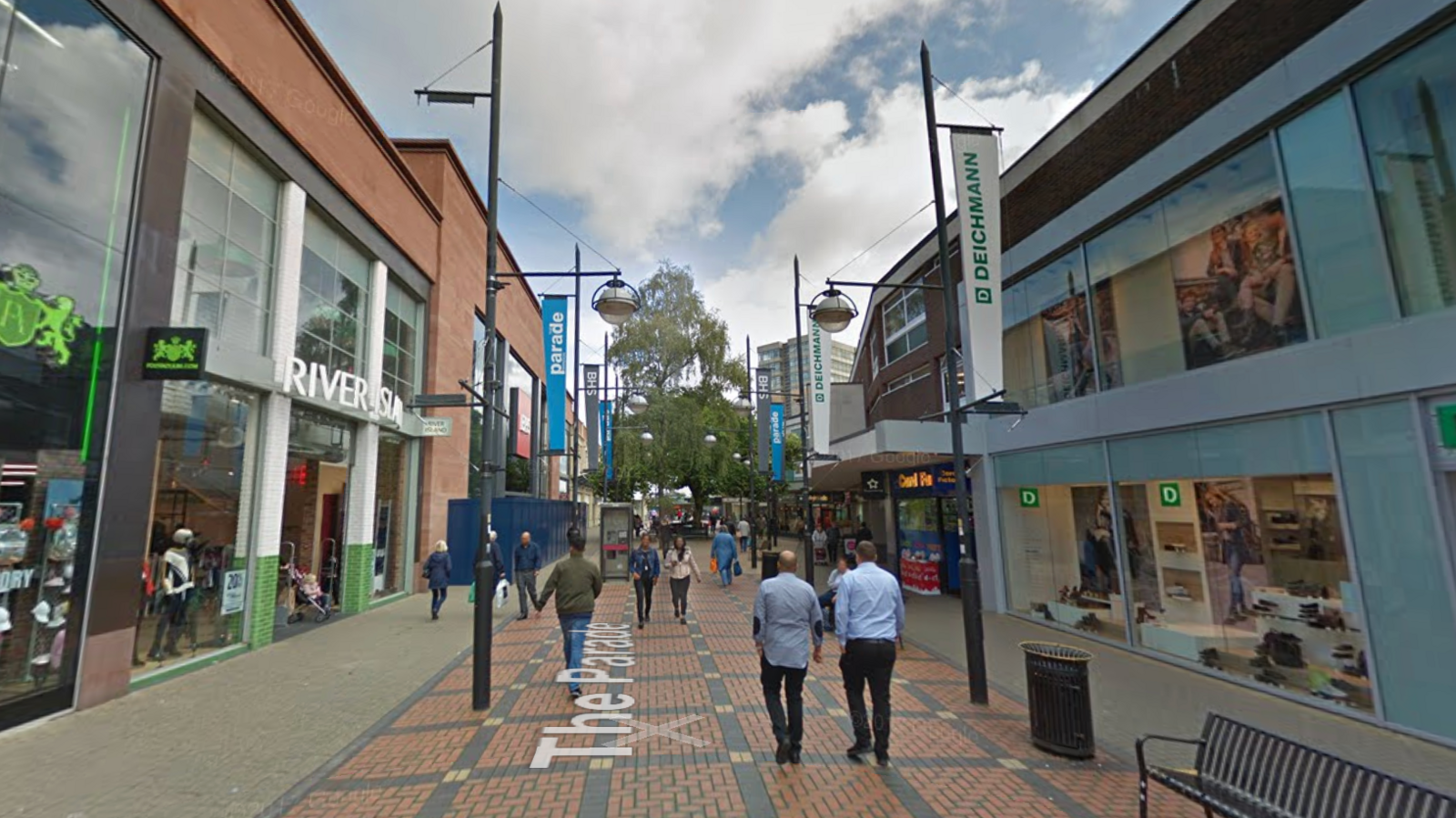 The Parade in Swindon. Shops can be seen either side of the street, as well as benches, flags and people. 