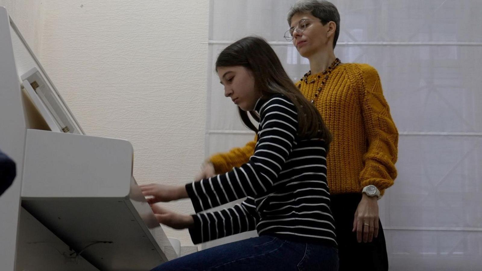 A girl called Anna wearing black and white striped long-sleeve top plays the piano