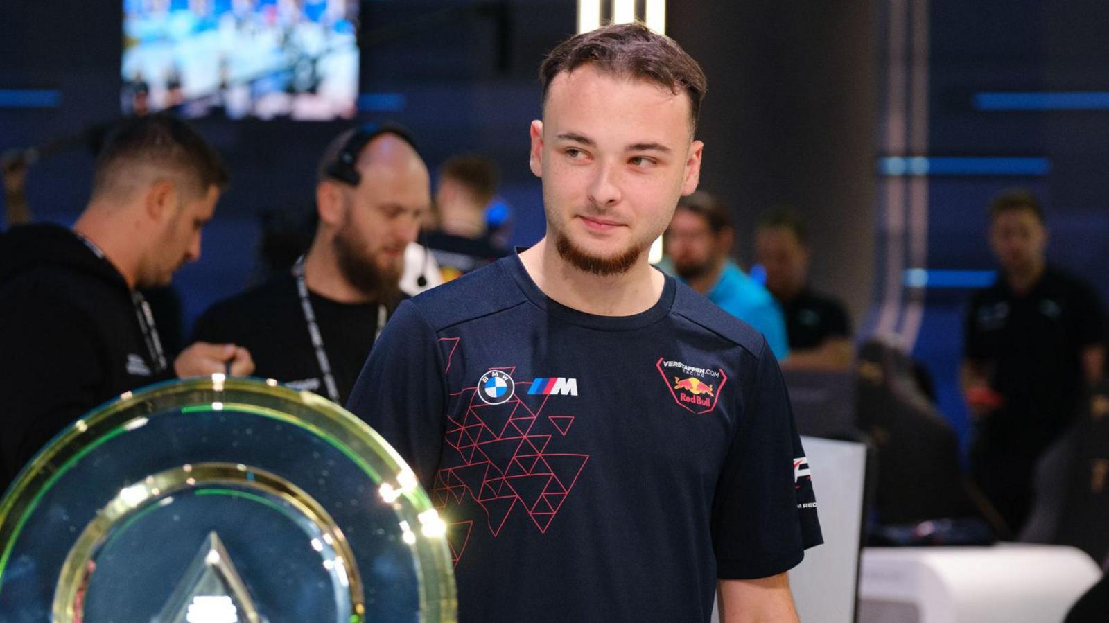 Luke Bennett, pictured with a trophy at the Esports World Cup in Saudi Arabia.  Luke is a 19-year-old man with short brown hair and a short goatee beard. He wears a black T-shirt. 