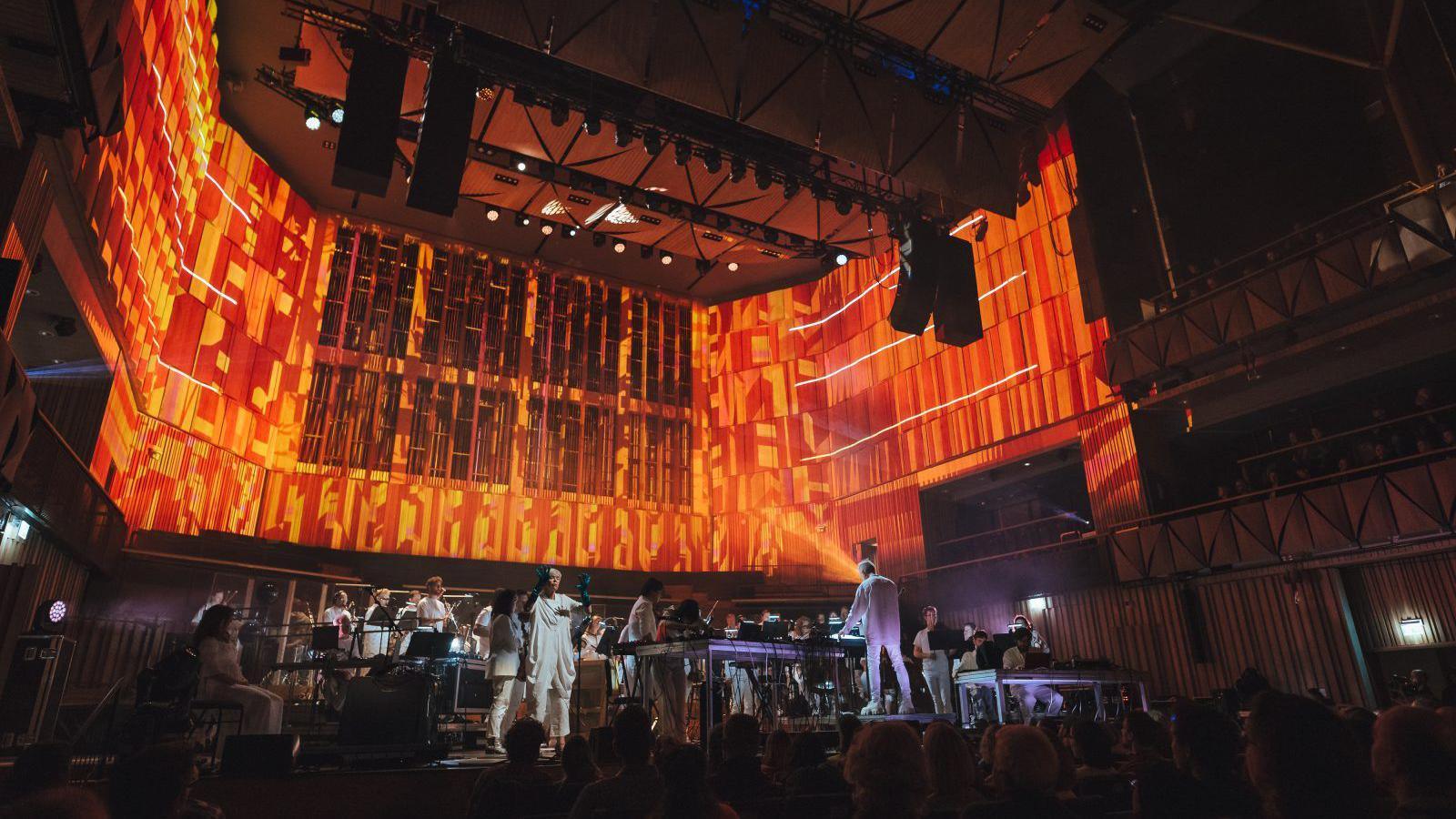 Paraorchestra on stage at Bristol Beacon, with orange and purple lighting