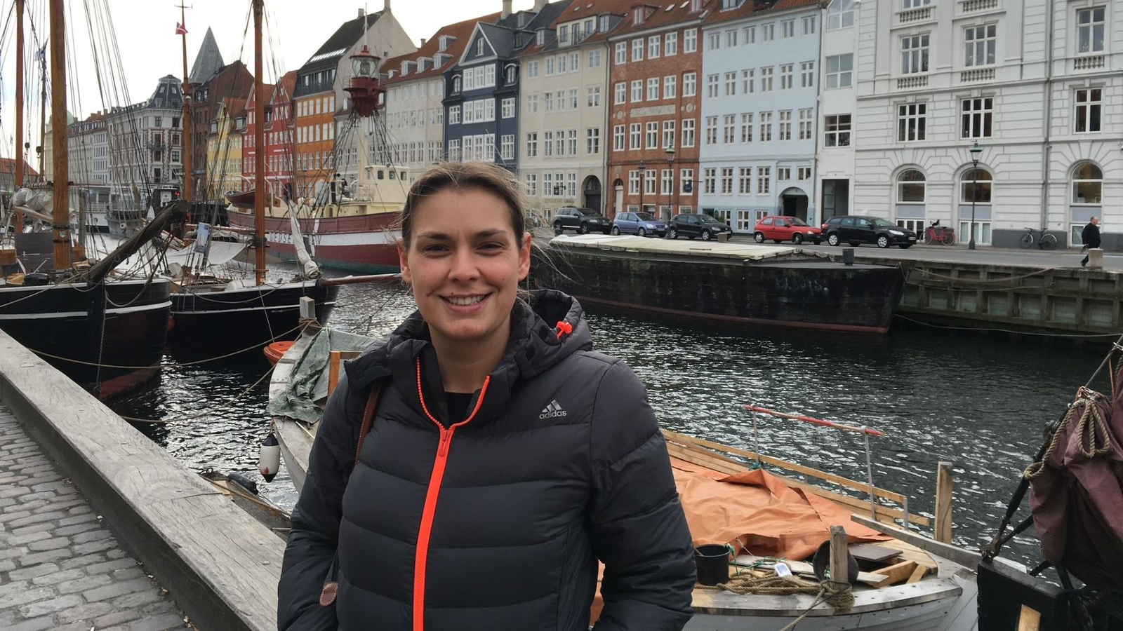 A picture of Tarryn Baird, standing in front of a canal or river, wearing a coat and smiling at the camera. 