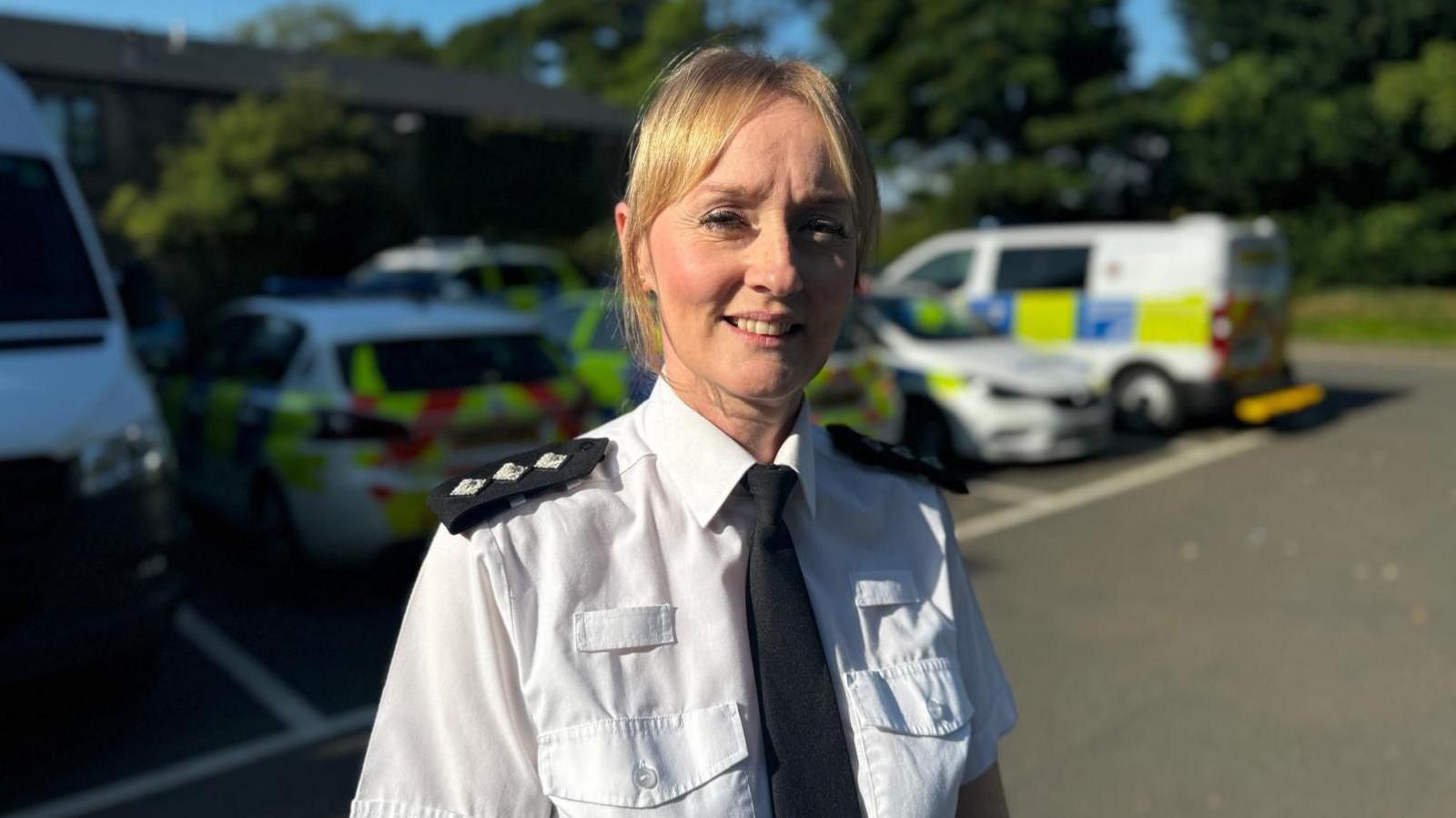 Ch Insp Gemma Calvert in police uniform, smiling at the camera with police vehicles in the background