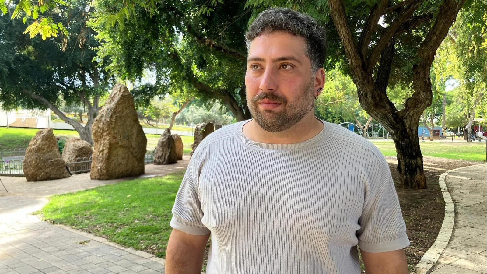 Noam Glukhovsky stands outside in a park wearing a beige T-shirt