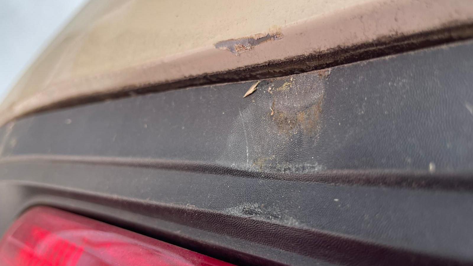 The dented and scratched rear bumper of a Mini. The paintwork has been scratched away above the dented plastic.