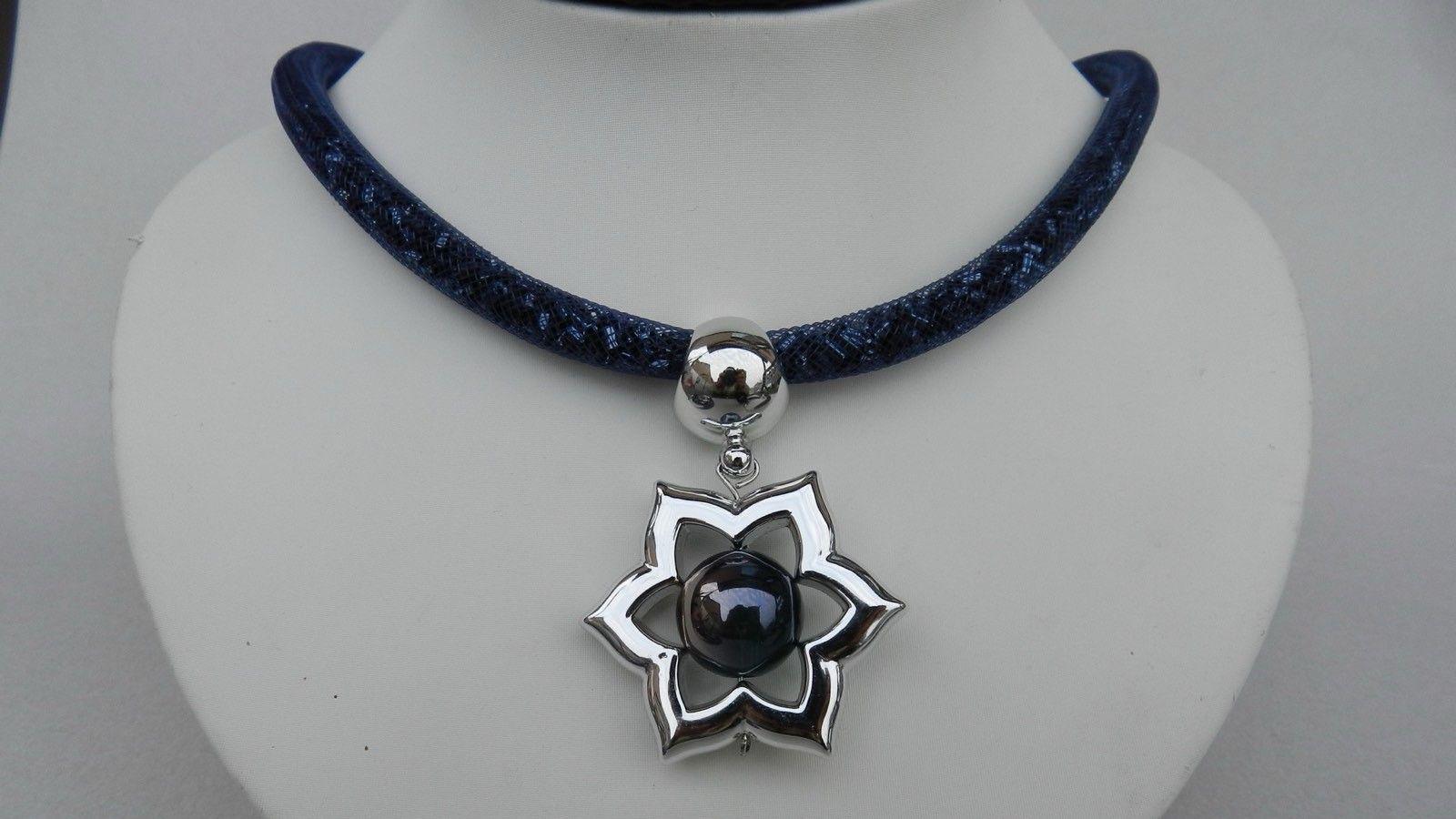 A necklace rests on a jewellery bust. It has a dark blue fabric cord that sits around a person's neck and a metal flower hangs from it with a circular stone in the middle of it.
