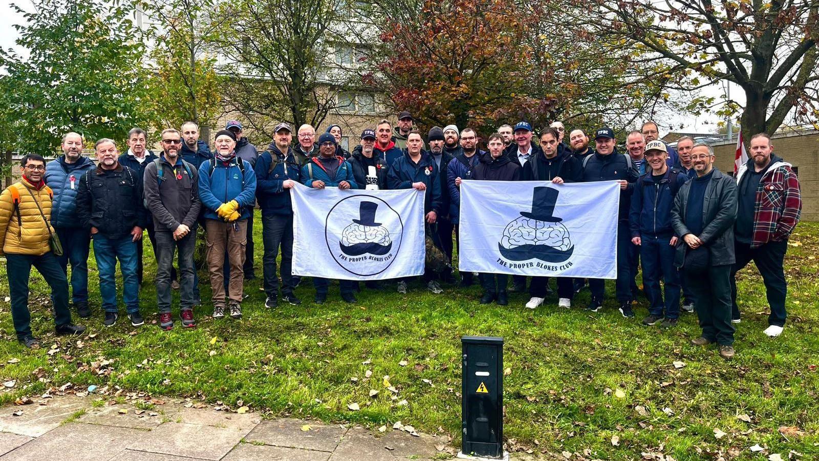 A group of men holding two banners with the Proper Blokes Club logo.