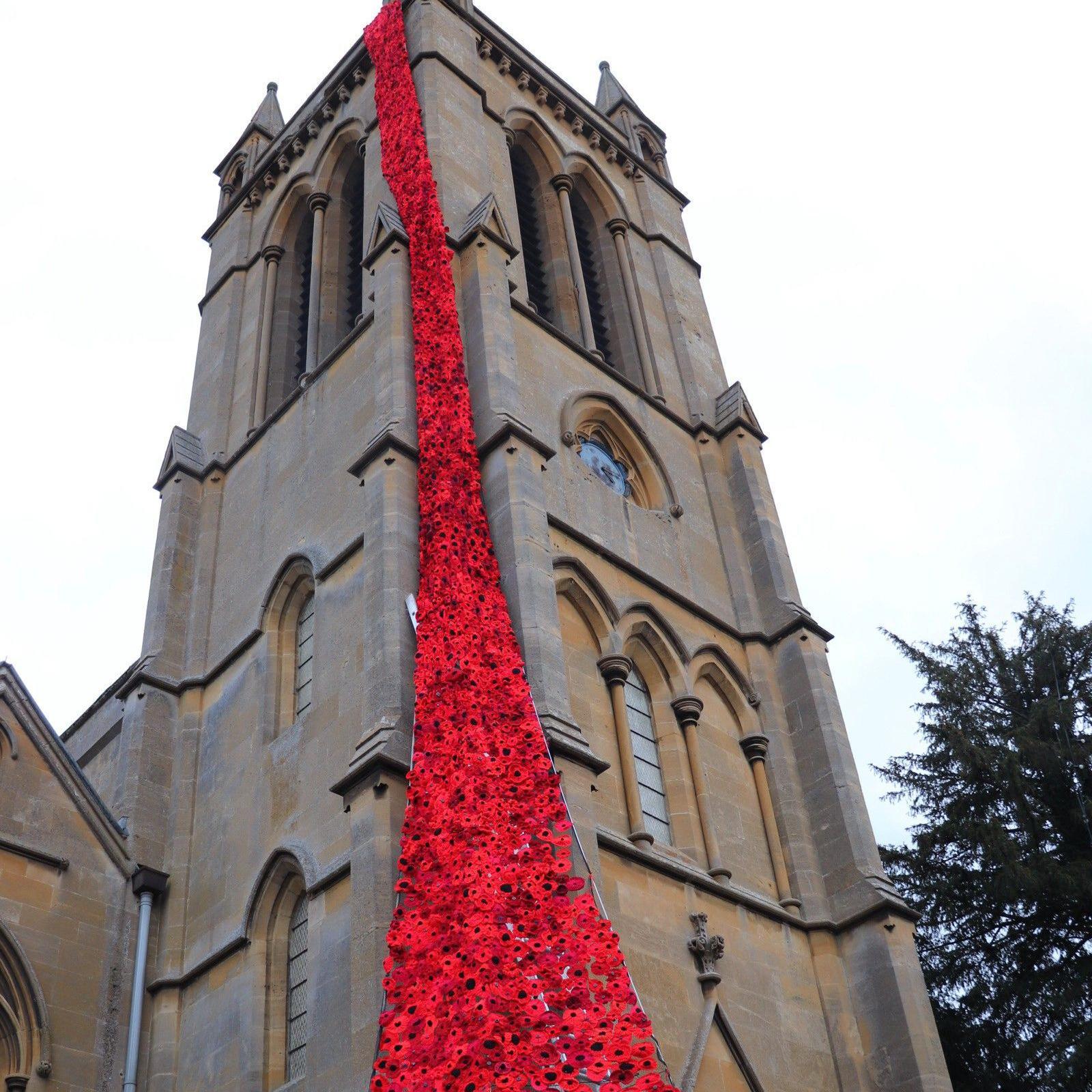 Knitted poppies on the corner of a church tower, beginning at the top near the roof and going all the way down to the ground.
