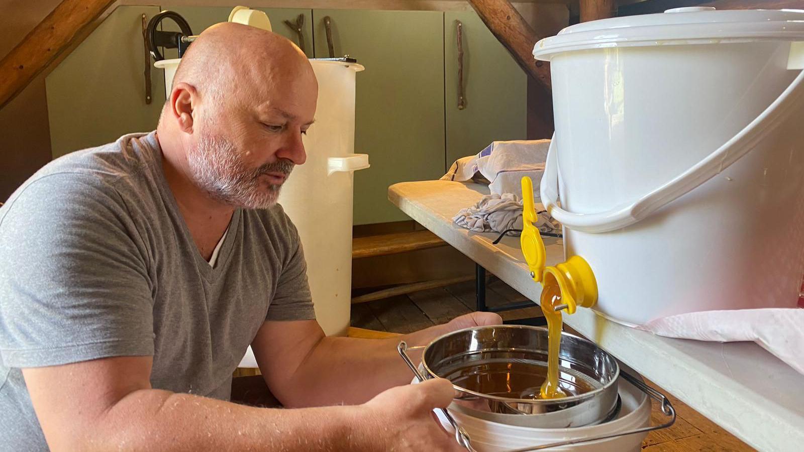 Salvatore Scotti empties honey into a metal bowl from a plastic container's tap