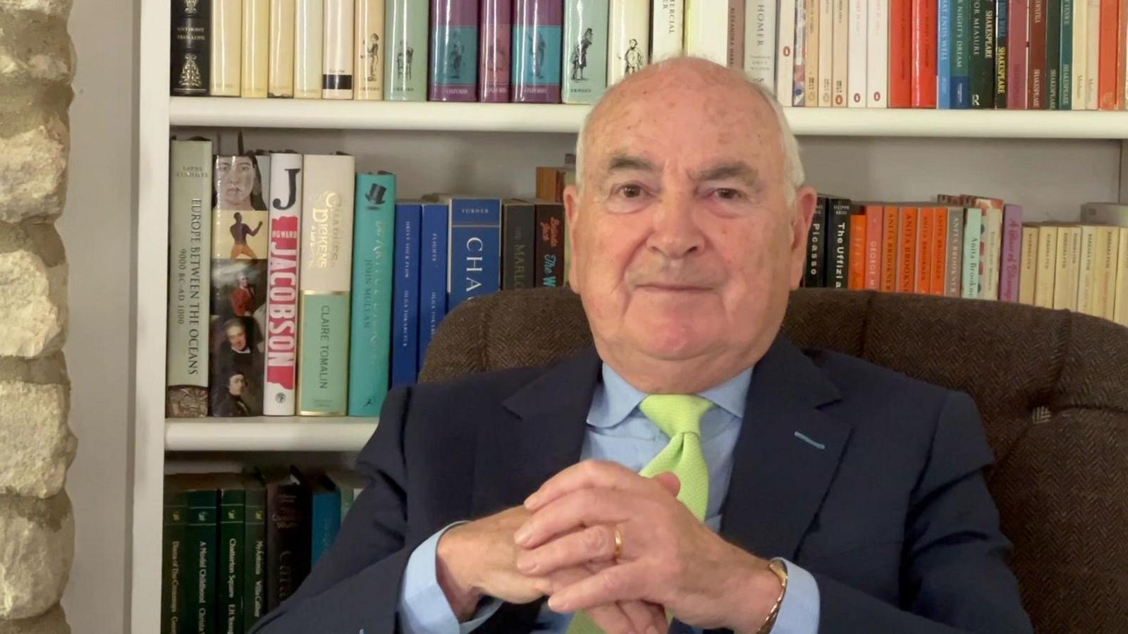 Man sat in chair in front of a bookcase