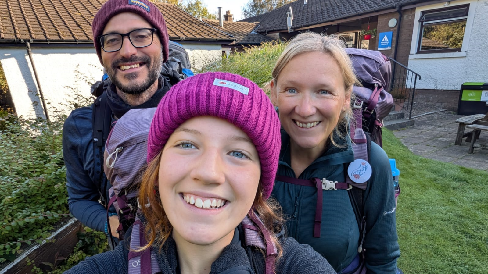 Tara (right), Matt (left) and Amelie's younger sister in the centre. They are all wearing walking gear outside and smiling at the camera.