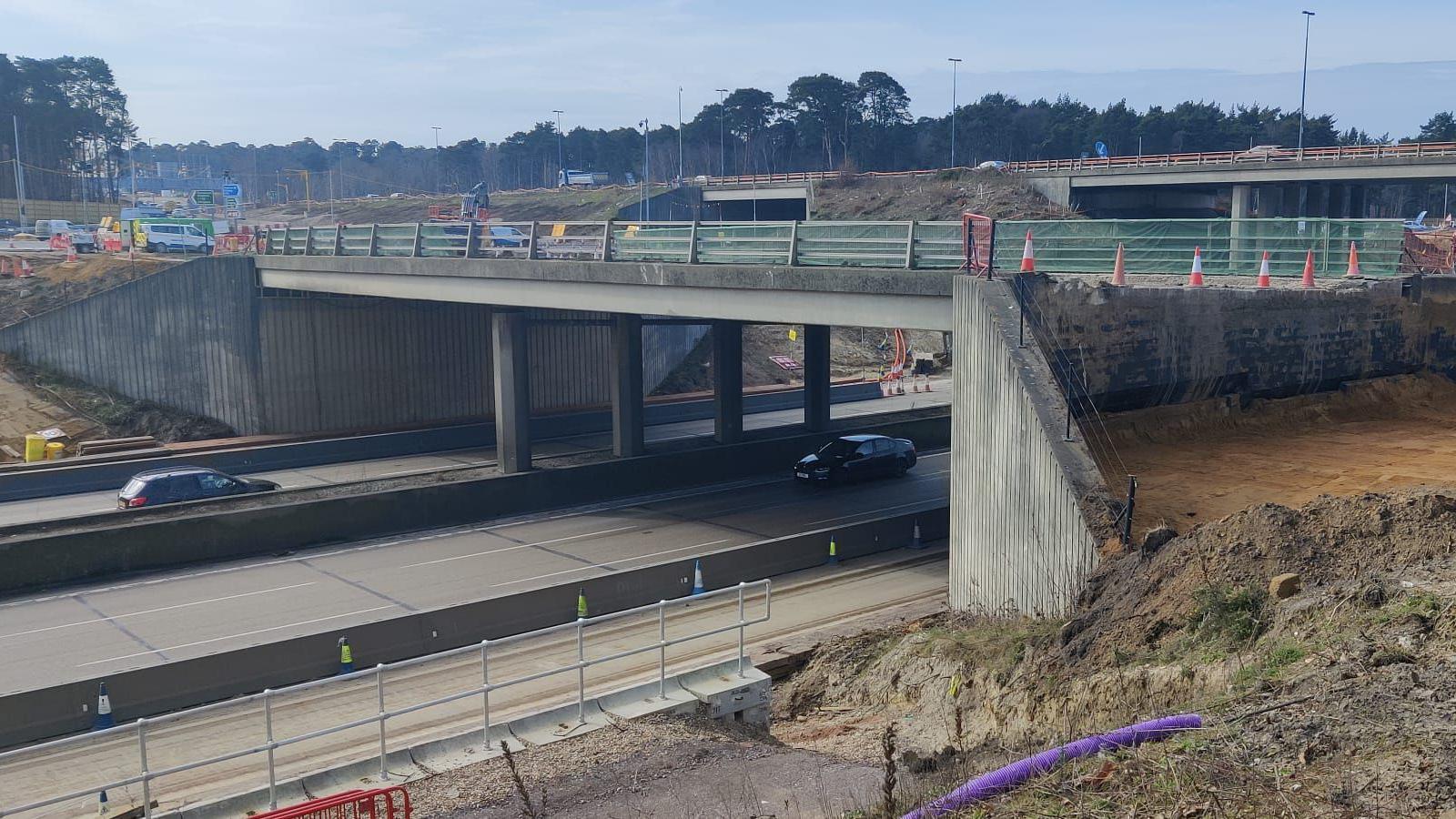 A concrete bridge over a motorway which has been fenced off with orange cones  lining an abrupt end of road.