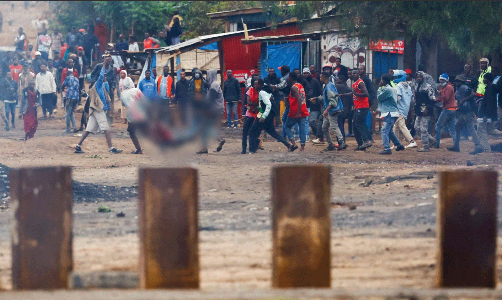 A protest scene in Tanzania, a crowd of men, a casualty being carried