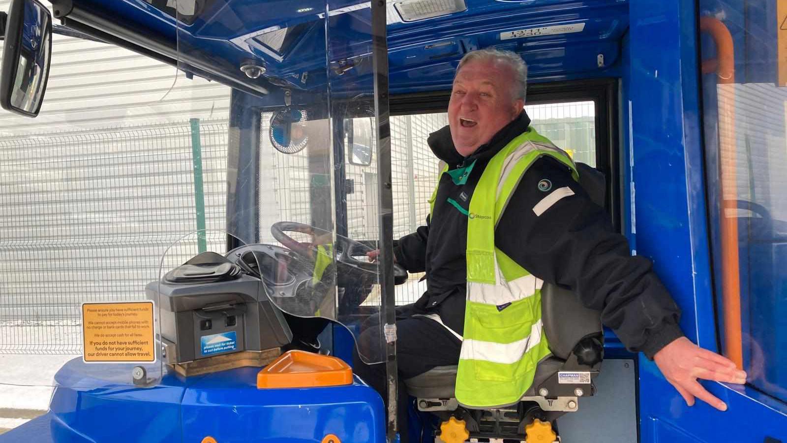 Michael Fletcher laughs while sat in the driver's seat on-board a Magic Bus, which is painted blue. 