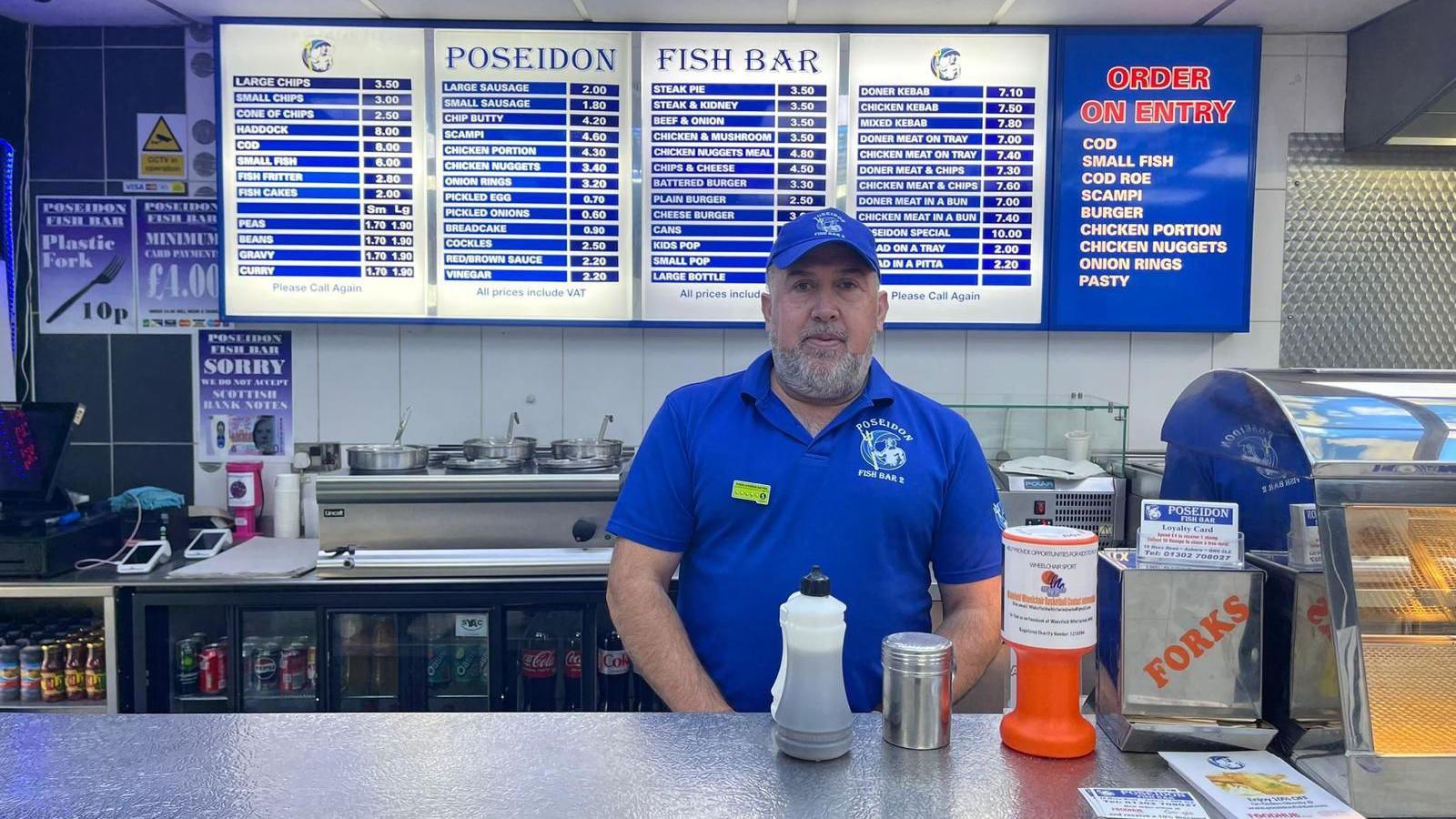 A man behind the counter of a takeaway with menus in the background
