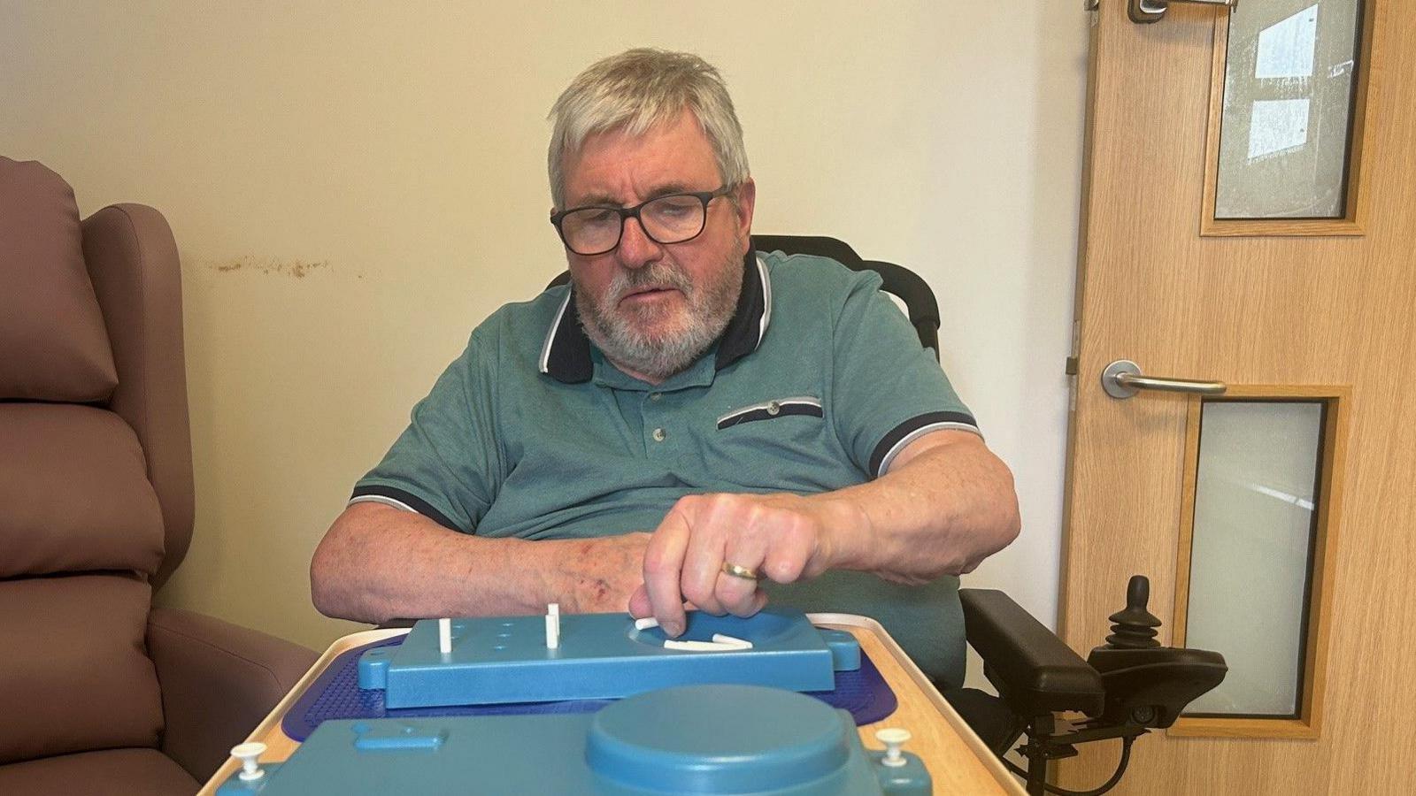 A man in a blue polo shirt sitting in front of a blue tray with white pegs
