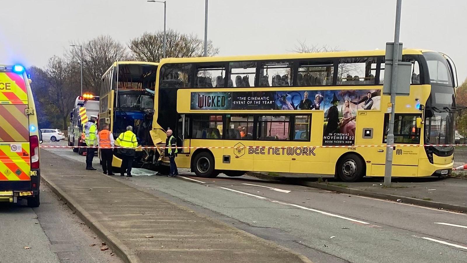 A damaged Bee Network bus with a shattered display board behind another Bee Network bus, taped off, which emergency workers pick through debris.