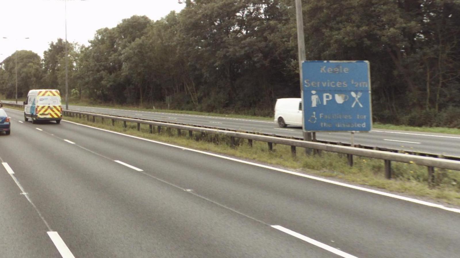 A picture of the M6, with vehicles travelling along it. A blue sign is located on the central reservation.