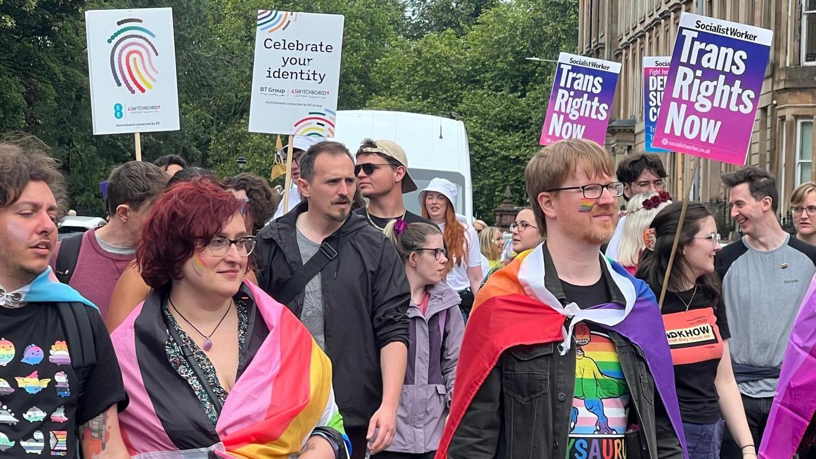 Pride marchers in Glasgow wearing colourful clothes and carrying Trans rights banners
