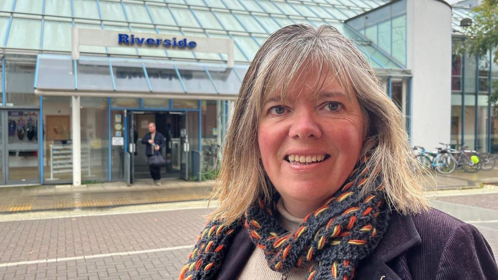 Exeter City Council's Green Party leader Diana Moore standing in front of the entrance to the Riverside Leisure Centre, wearing a knitted scarf and a purple jacket.