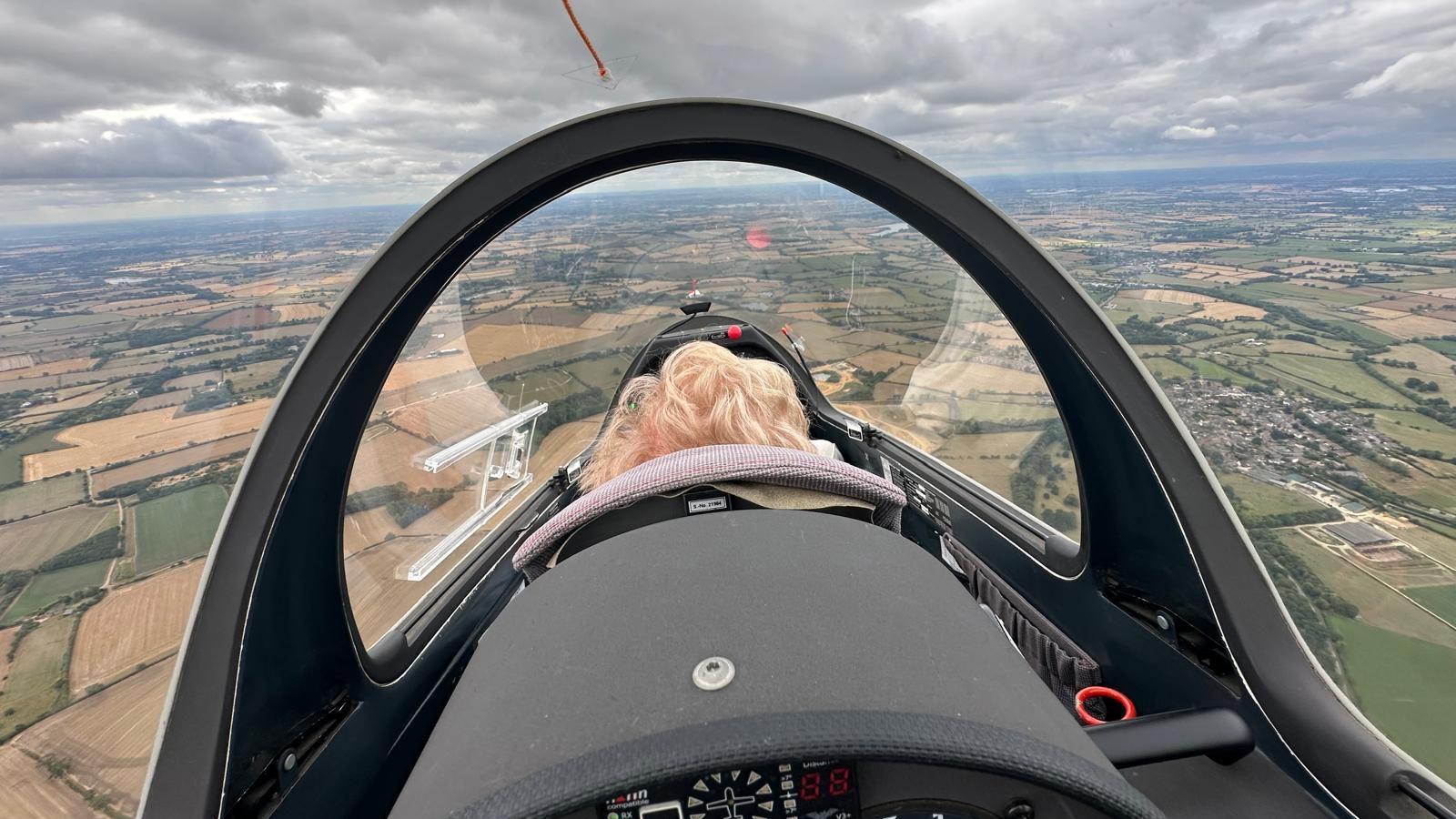 The back of Nora's head in the glider cockpit, with a view of Leicestershire below 