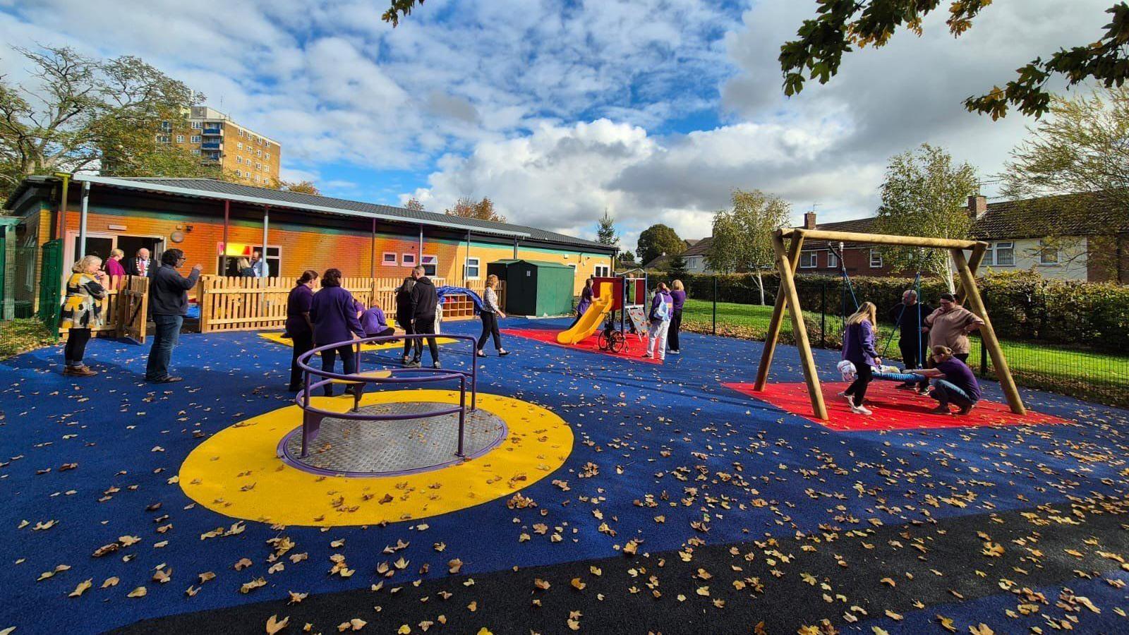 An outdoor garden space with a swing, roundabout and slides and adults and children using the equipment 
