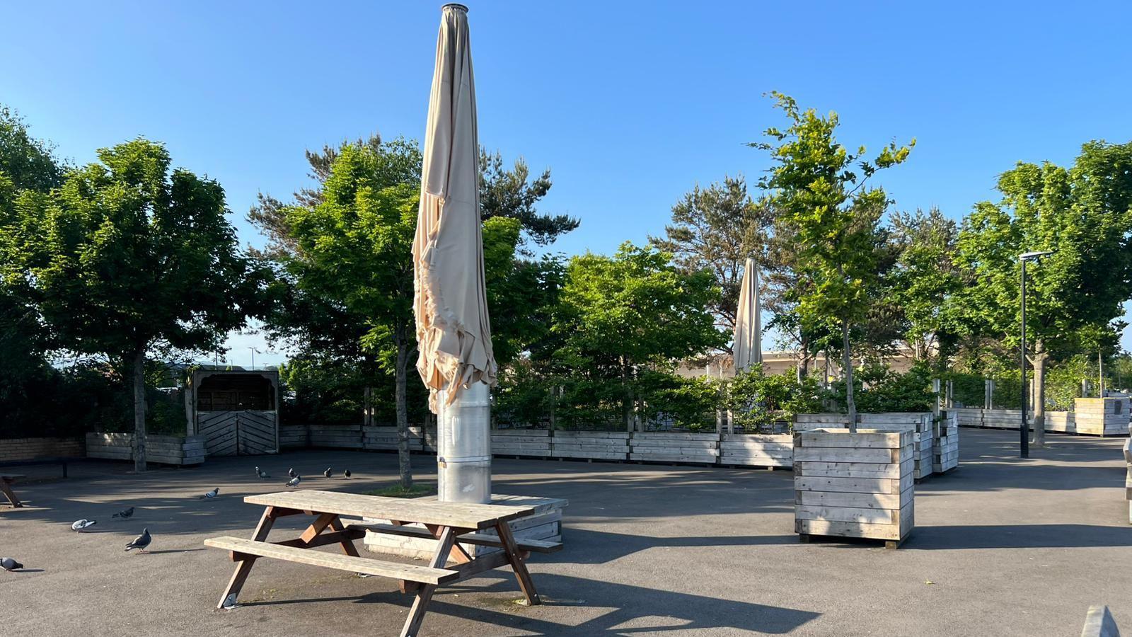 A number of items of street furniture including planters and picnic tables sit in an area close to the River Foyle's edge.