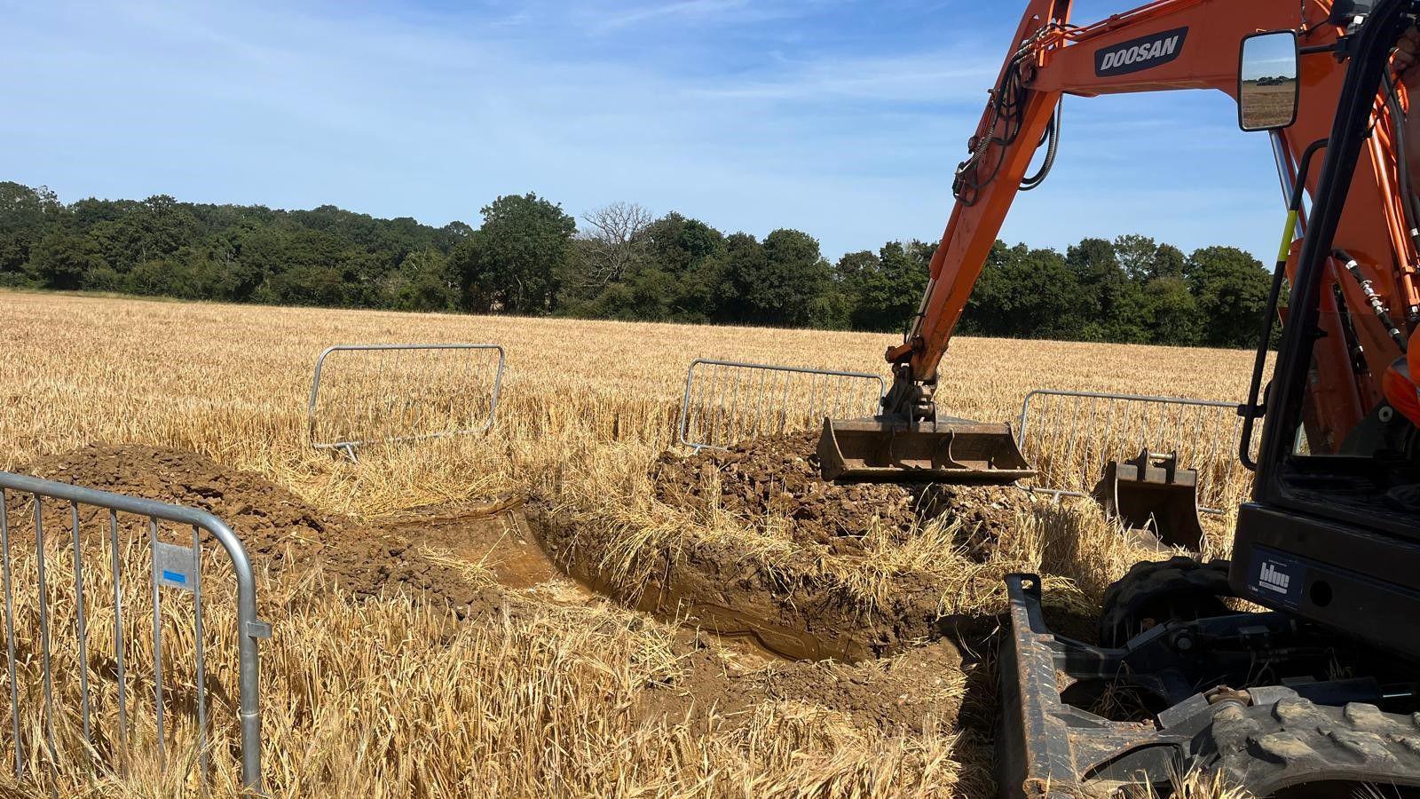 Digger in farmland with flattened barley crops