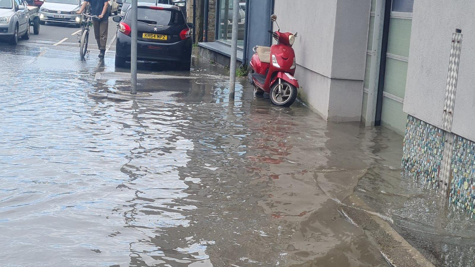 A street flooded with water, with a red scooter parked on the edge of the water