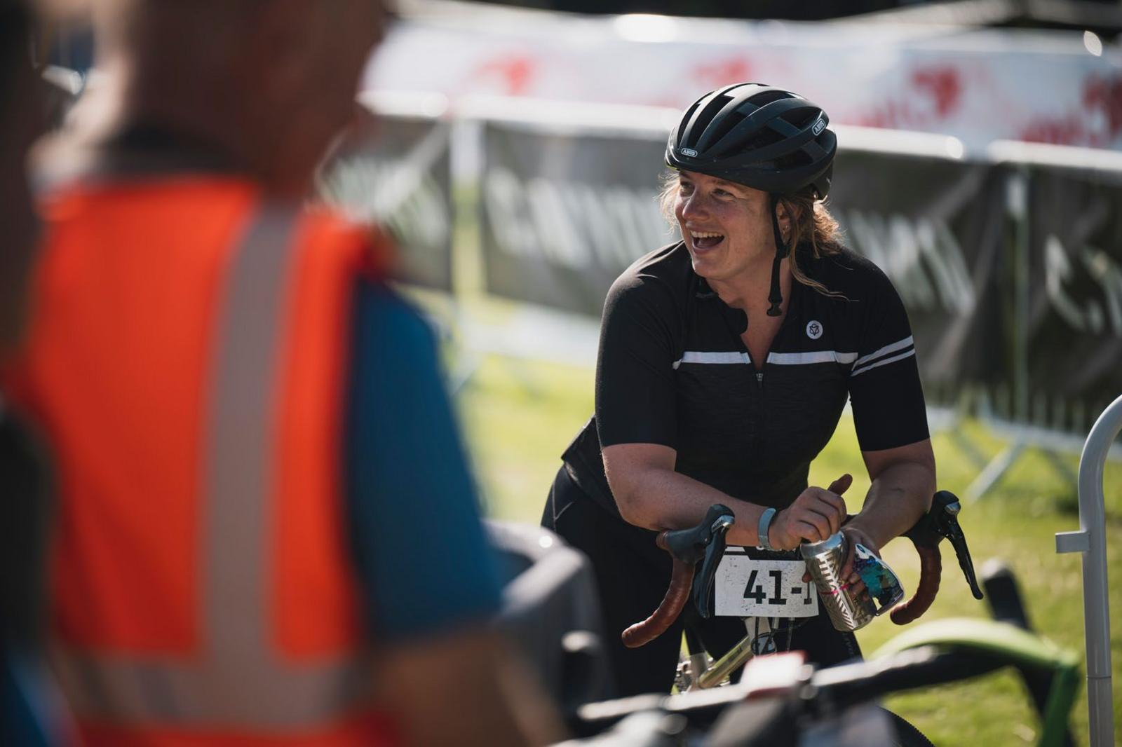 A woman on a bike with her helmet unbuckled takes a drink after completing a lengthy race