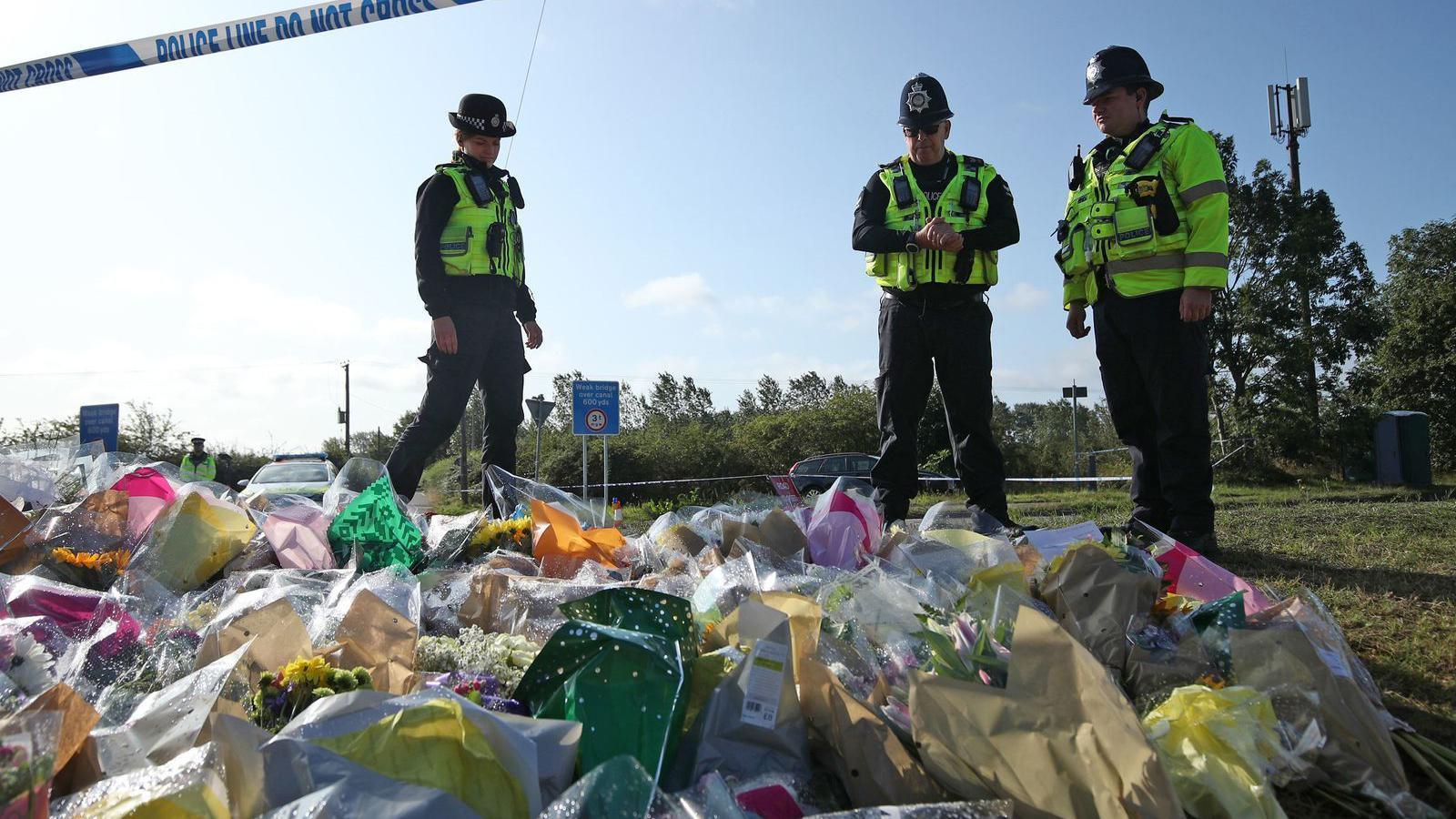 Three police officers stand by floral tributes to their colleague PC Andrew Harper