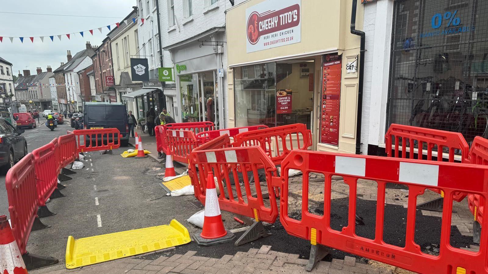 A different angle of the pavement, red barriers surround a restaurant shop front, with a yellow ramp