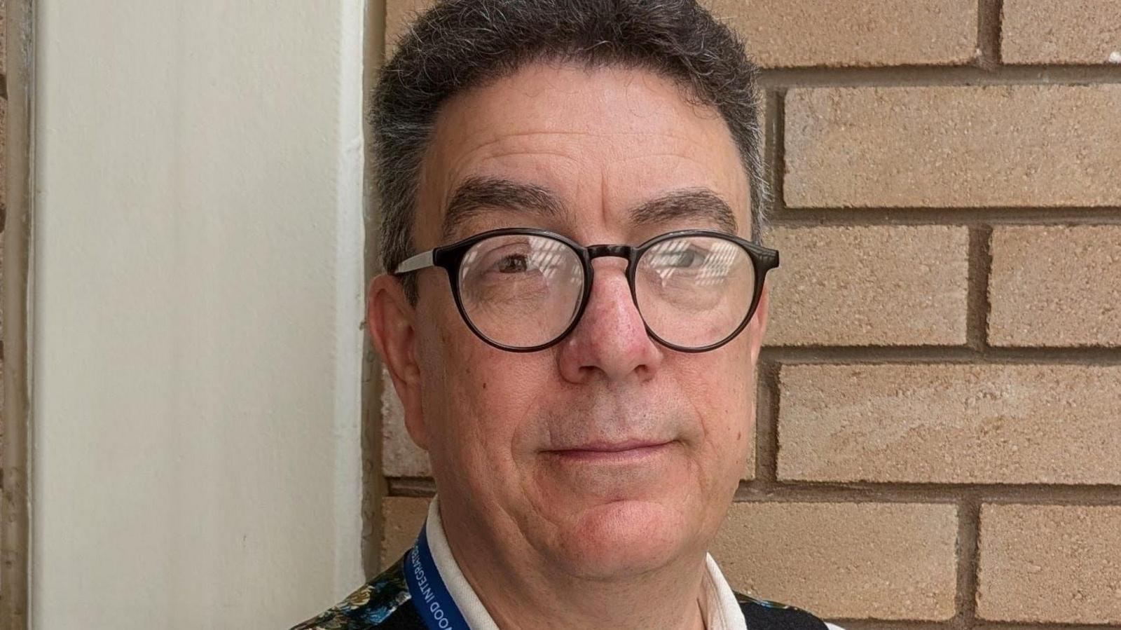 Brian has quirky round rimmed classes and thick hair that growing outwards, which he keeps quite short. One eyebrow is raised slightly in a quizzical way. 