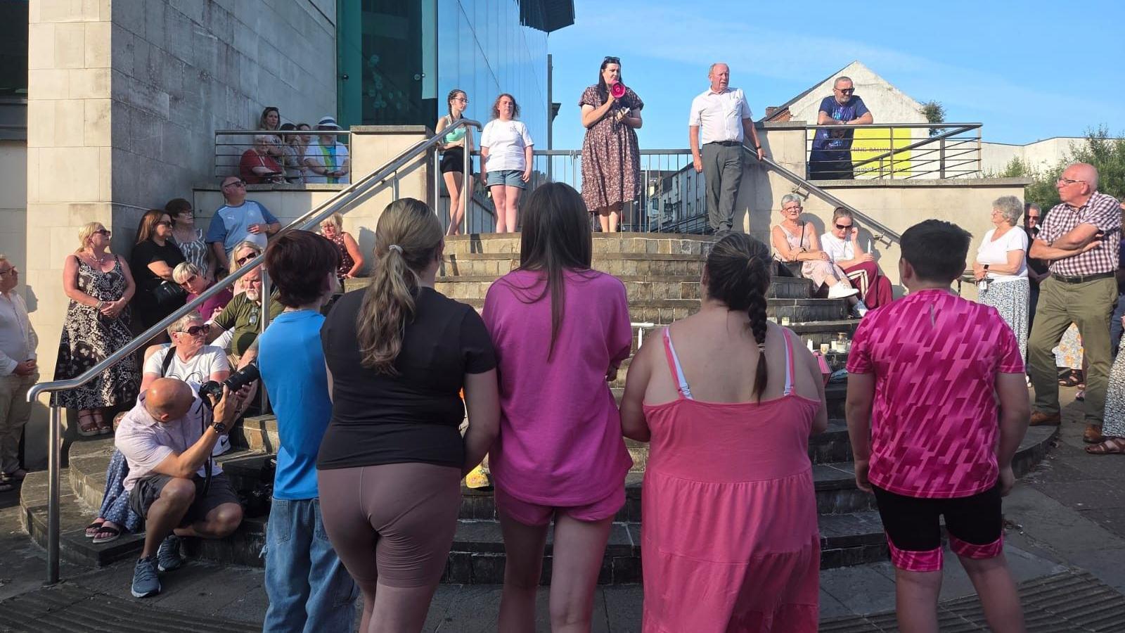 A group of people stand to pay their respects to the woman and child