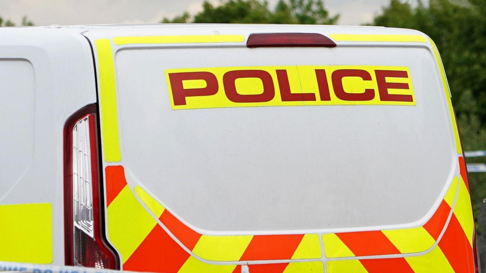 A general view of a police van. The van is white with orange and yellow trim. It has the word 'Police' on in red writing against a yellow background.