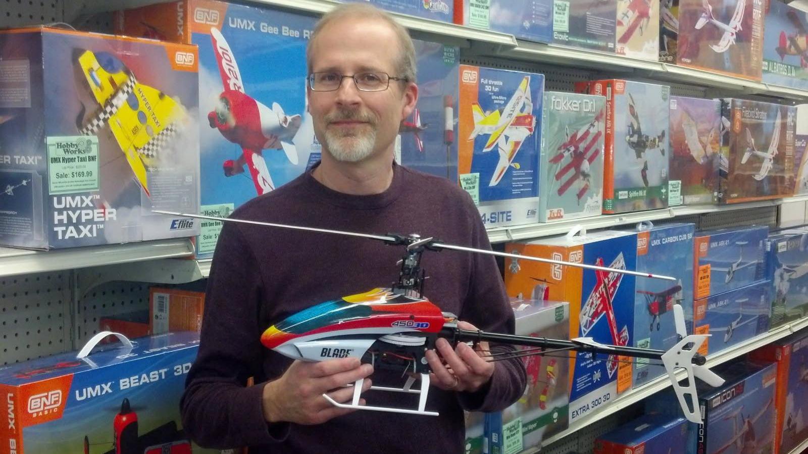 Michael Brey poses inside a toy store, holding a toy helicopter, with boxes of toy planes seen on the shelves behind him