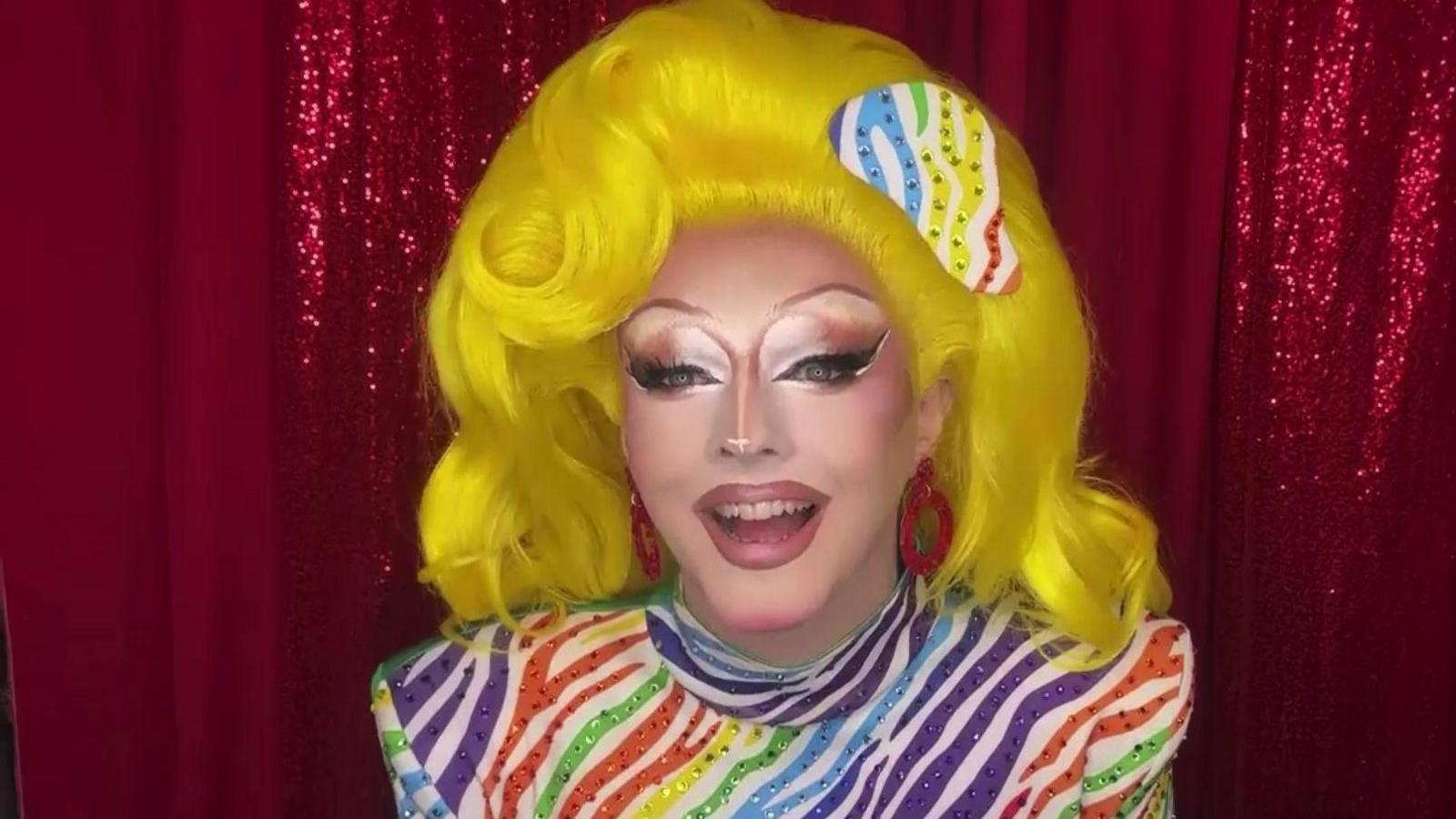 Charra Tea wears a bright yellow wig and dramatic neutral make up. She is wearing a multi-coloured zebra striped body suit with shoulder pads.