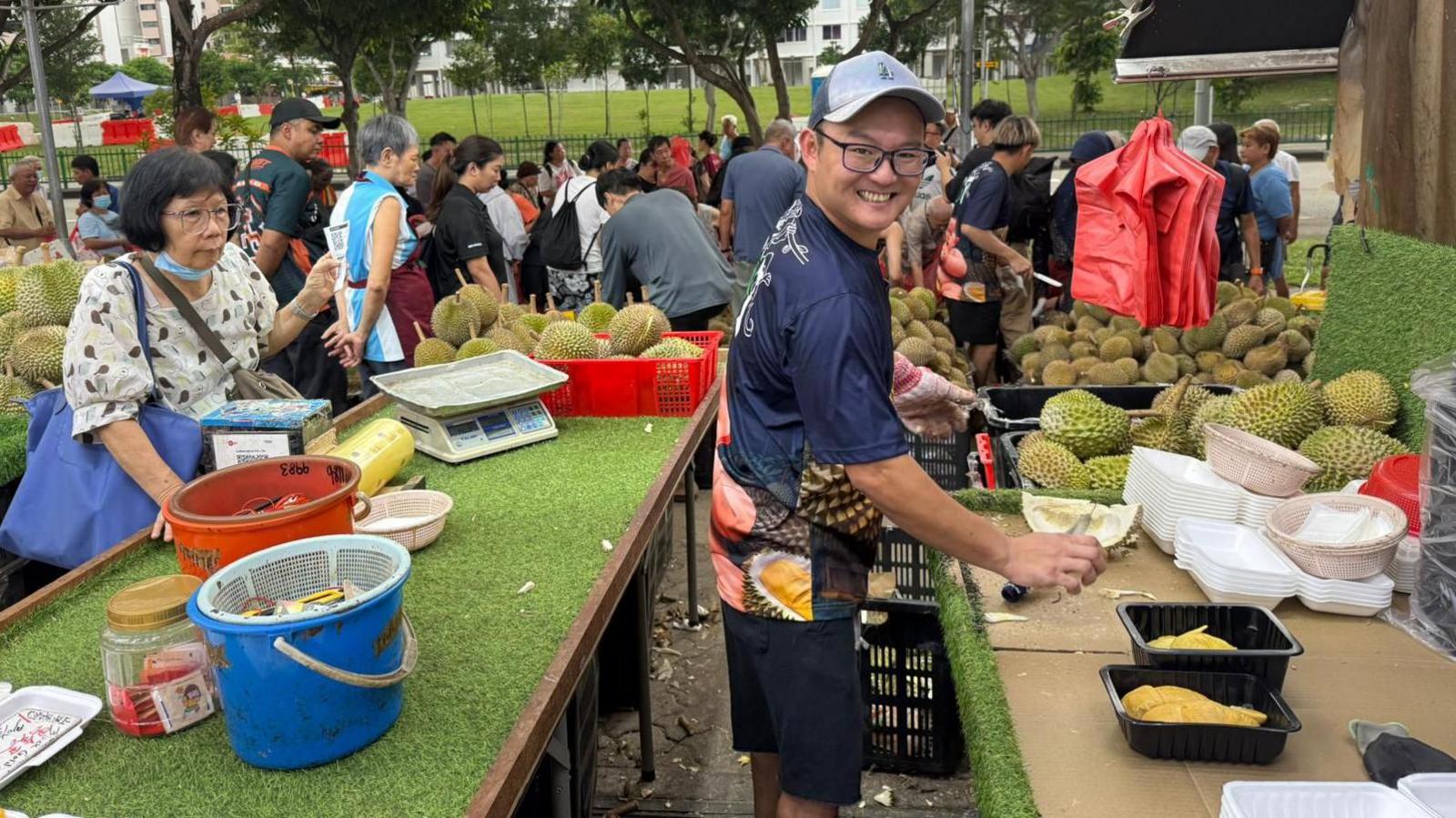 A man smiling at the camera as he cuts durian