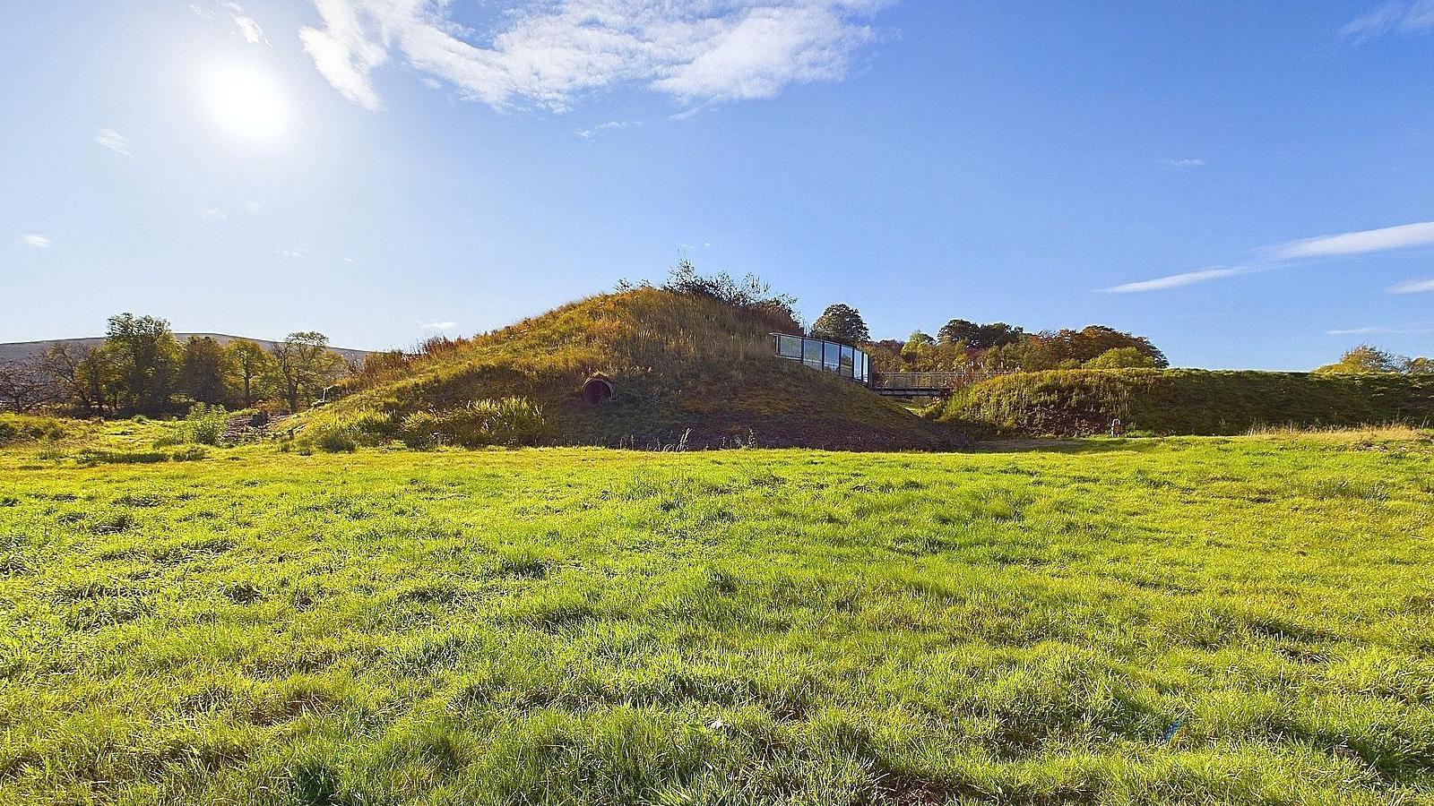 The Archaeolink Prehistory Park. The building is covered in grass and looks like a hill. Only a small section of glass identifies it as a building. 