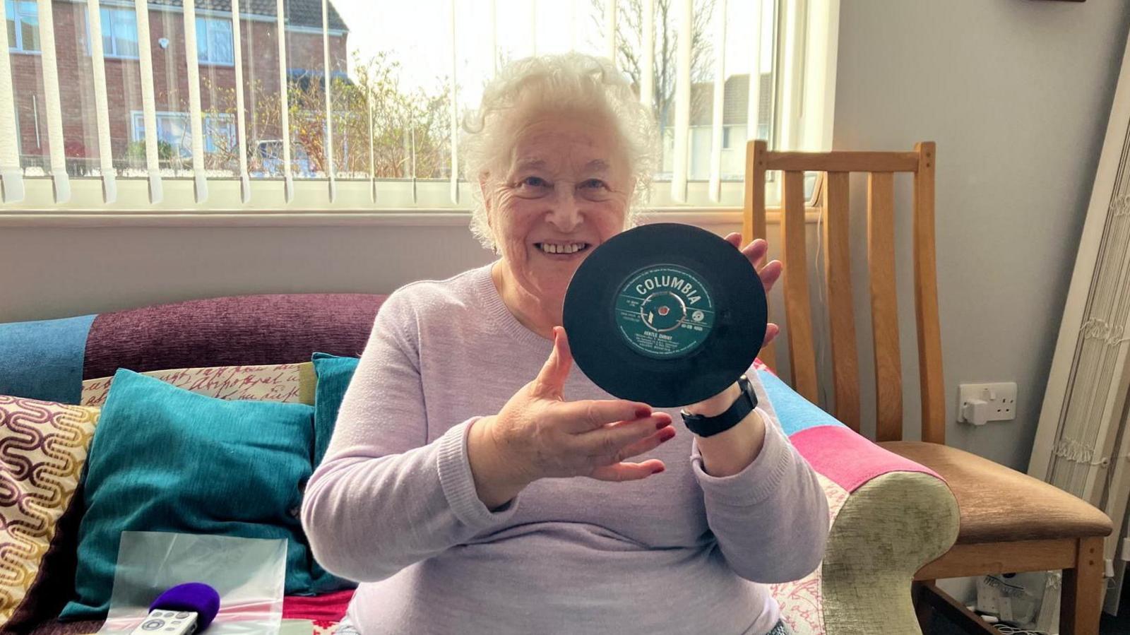 Christine Welsh who appeared in the original stage version of 'A Man Dies' sits in her living room and holds a seven inch record featuring two songs from the musical up to the camera