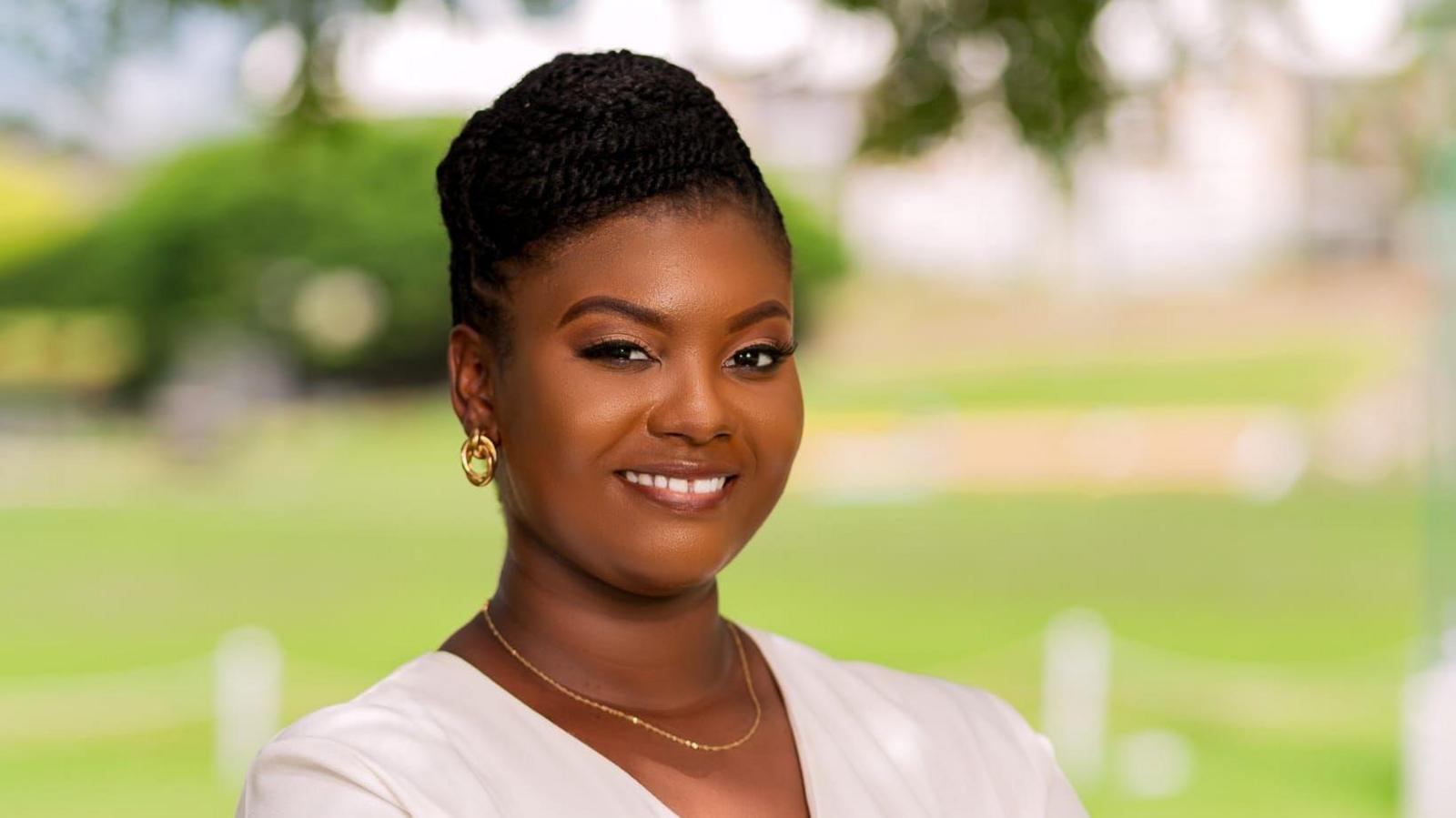 Brittney McKenzie, wearing gold hoop earrings,  a gold necklace and a white cardigan, poses for a photo