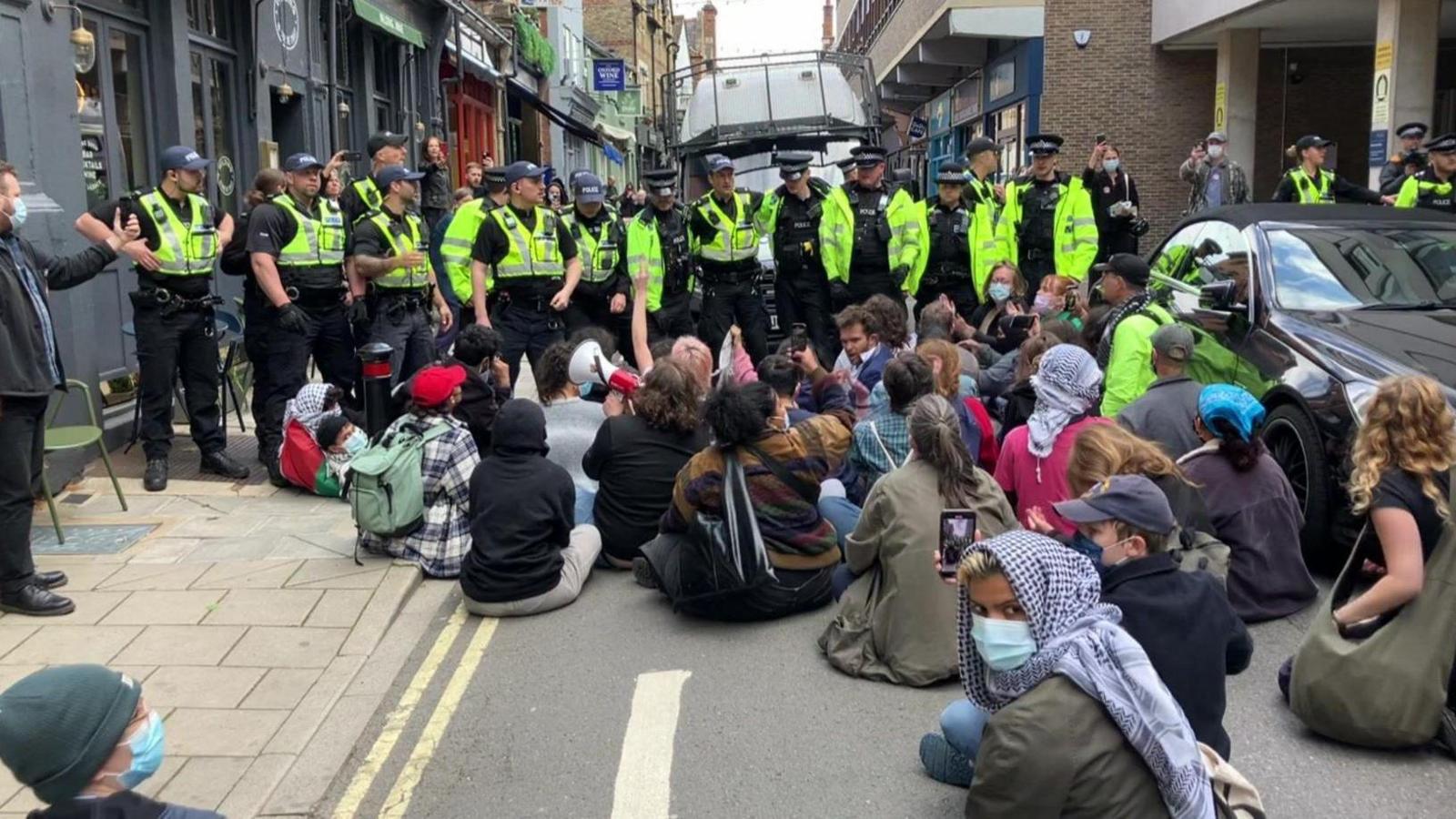 People sitting on the street in front of police.