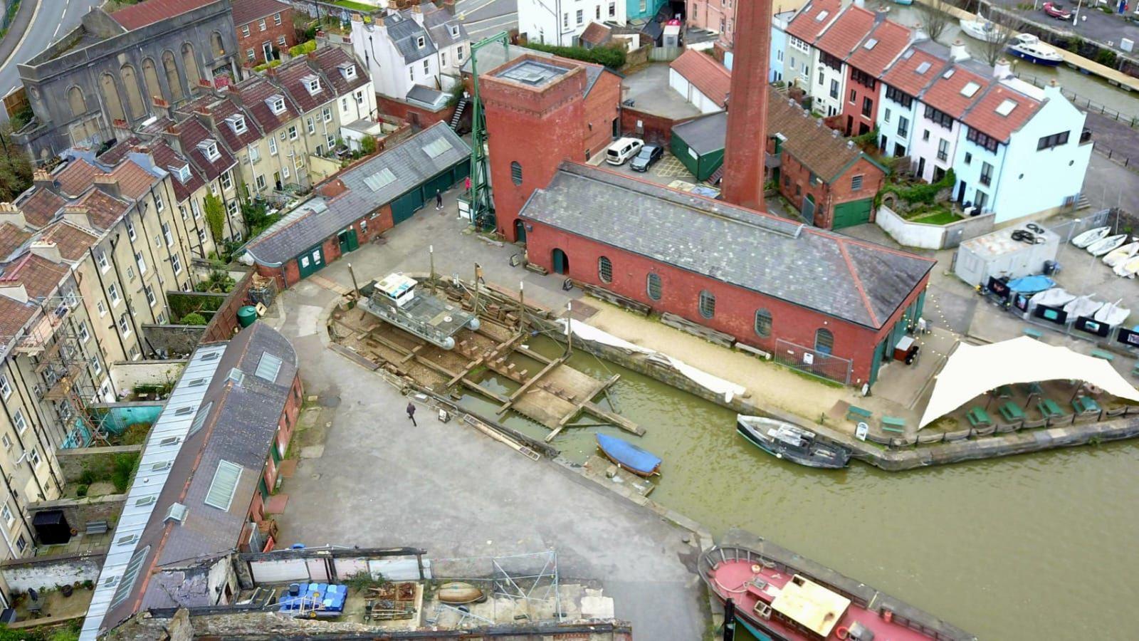 An aerial view of Underfall Yard in Bristol showing some small boats moored up and some damage from the arson attack it suffered. A cafe under a white awning is also visible