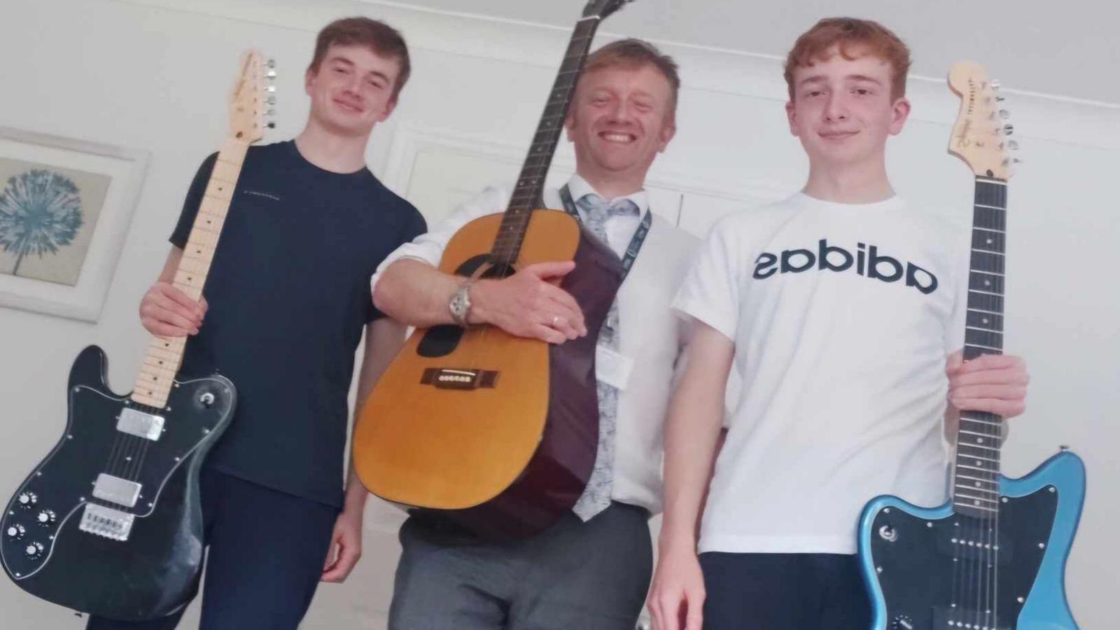 Terence Anthony and his two sons pose, smiling, with their guitars. They all have short ginger hair.