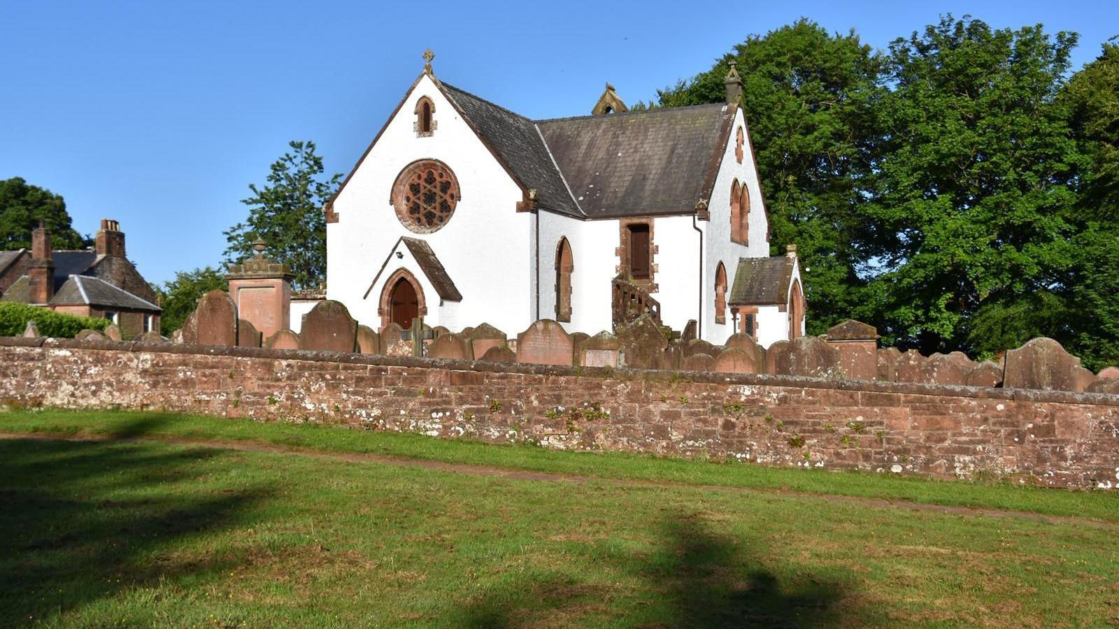 A whitewashed church with sandstone features around the windows, sitting on a hill surrounded by gravestones and a boundary wall