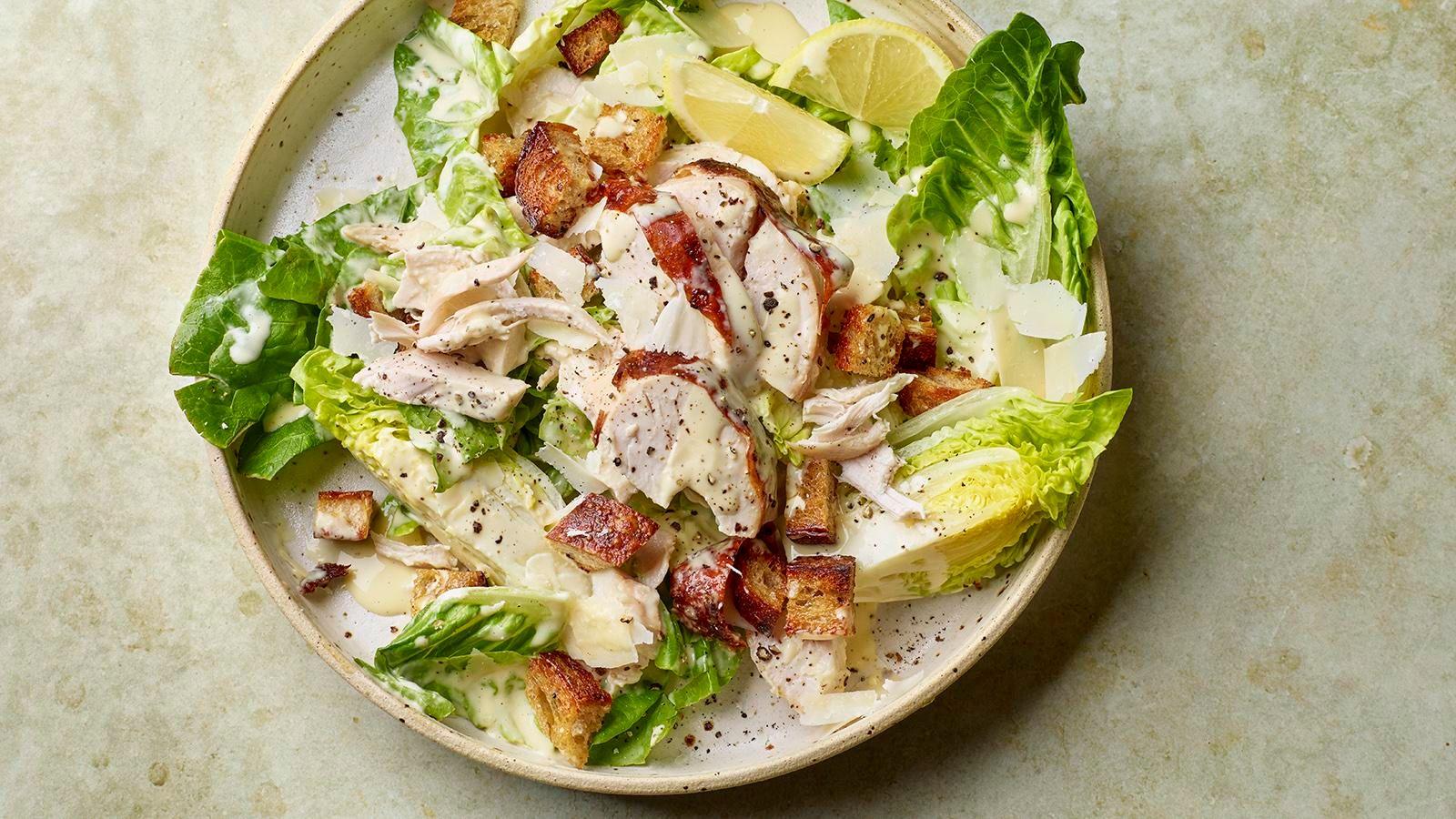 Caesar salad with chicken on top, in a bowl on a pale background