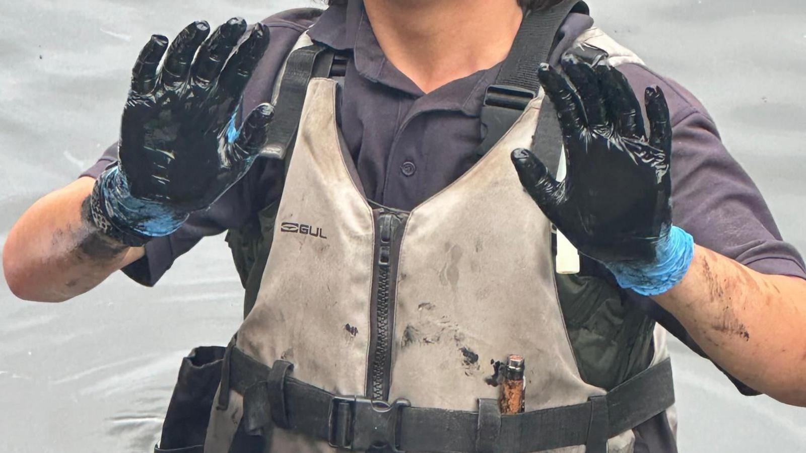 A swan support worker with black oil on their hands, which have gloves on