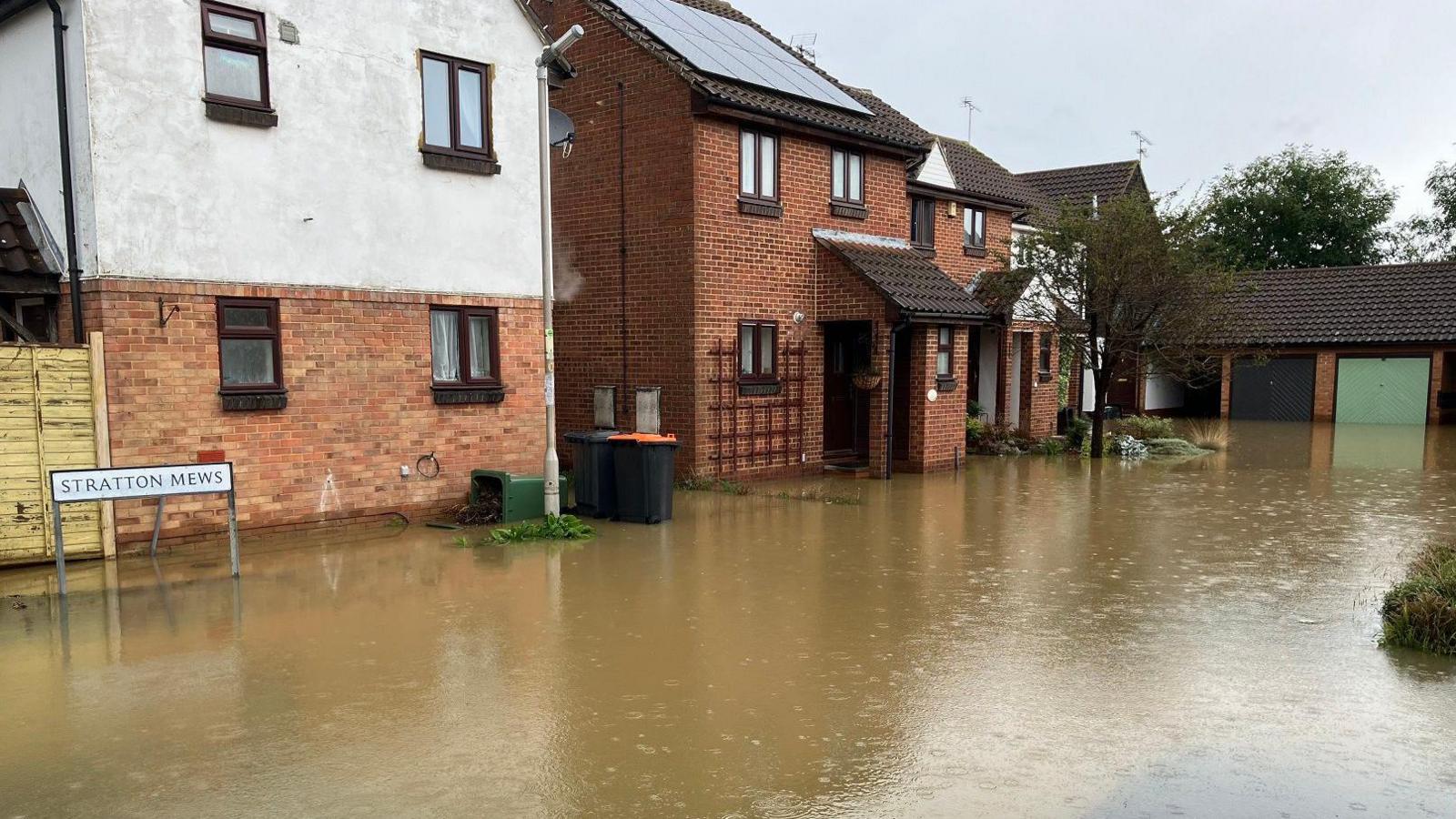 A row of houses on Stratton Mews in Leighton Buzzard, with the road in front flooded as rain falls.